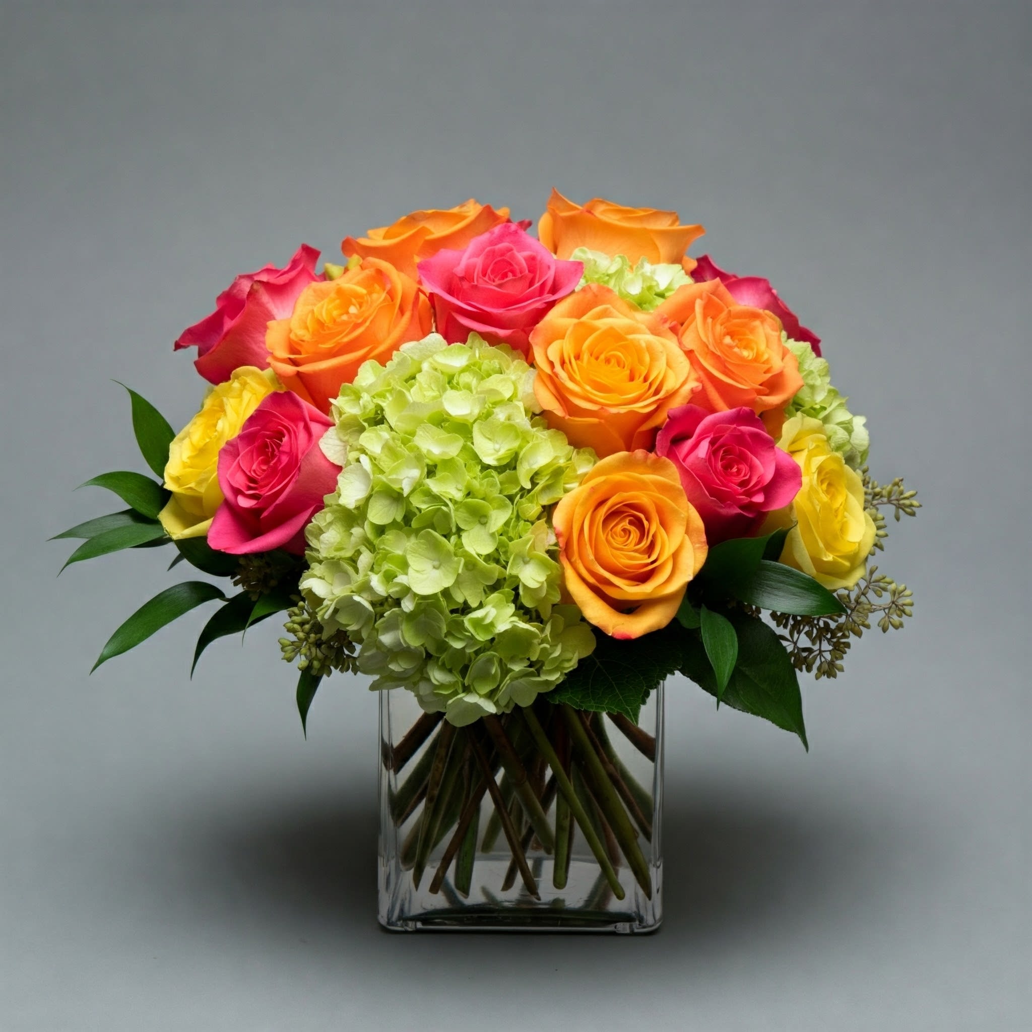 Bouquet of orange, pink, and yellow roses in a clear glass vase