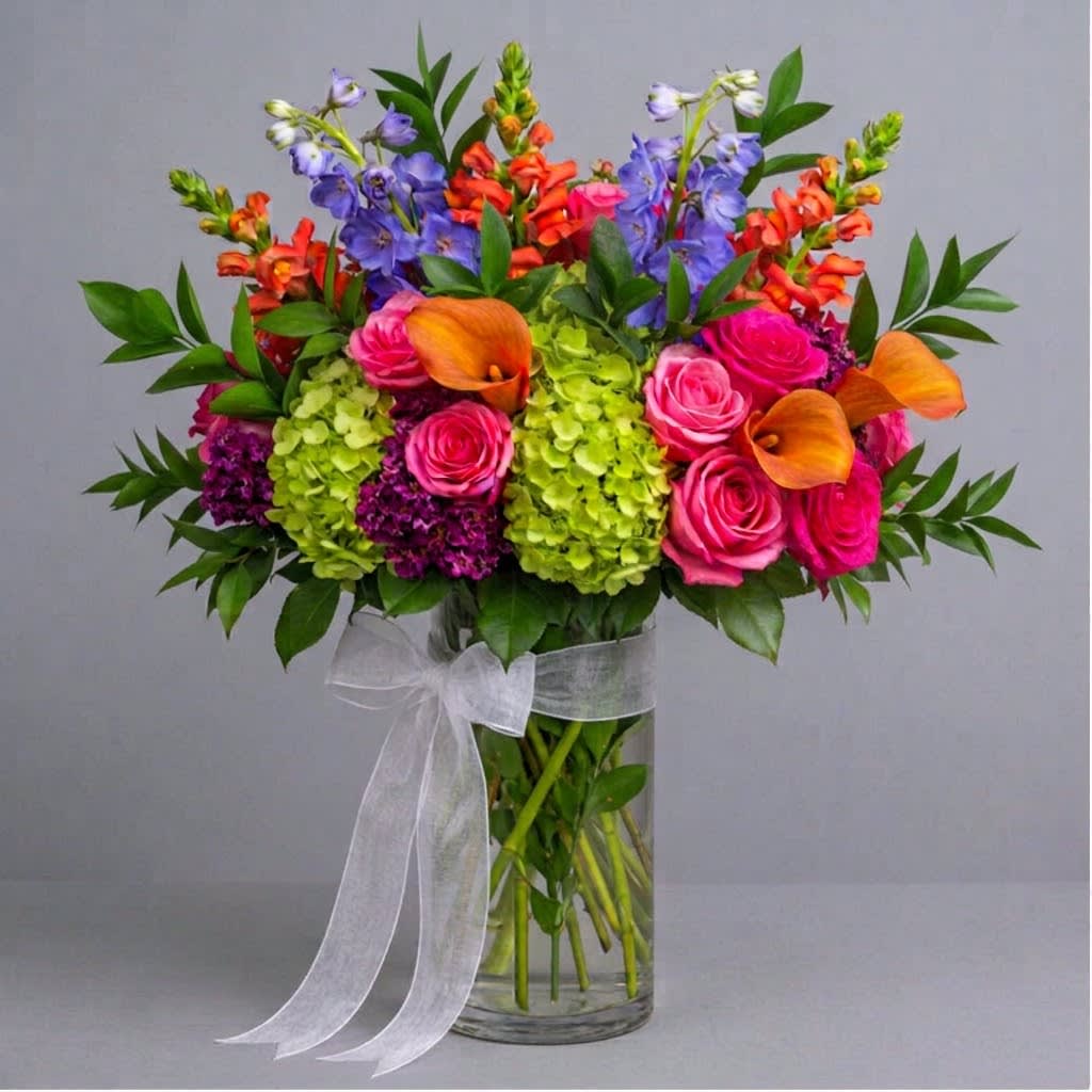 Bright mixed bouquet with pink roses, orange calla lilies, and purple blooms in a glass vase