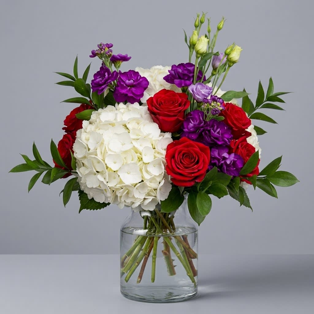 Bouquet of red roses, white hydrangeas, and purple flowers in a glass vase