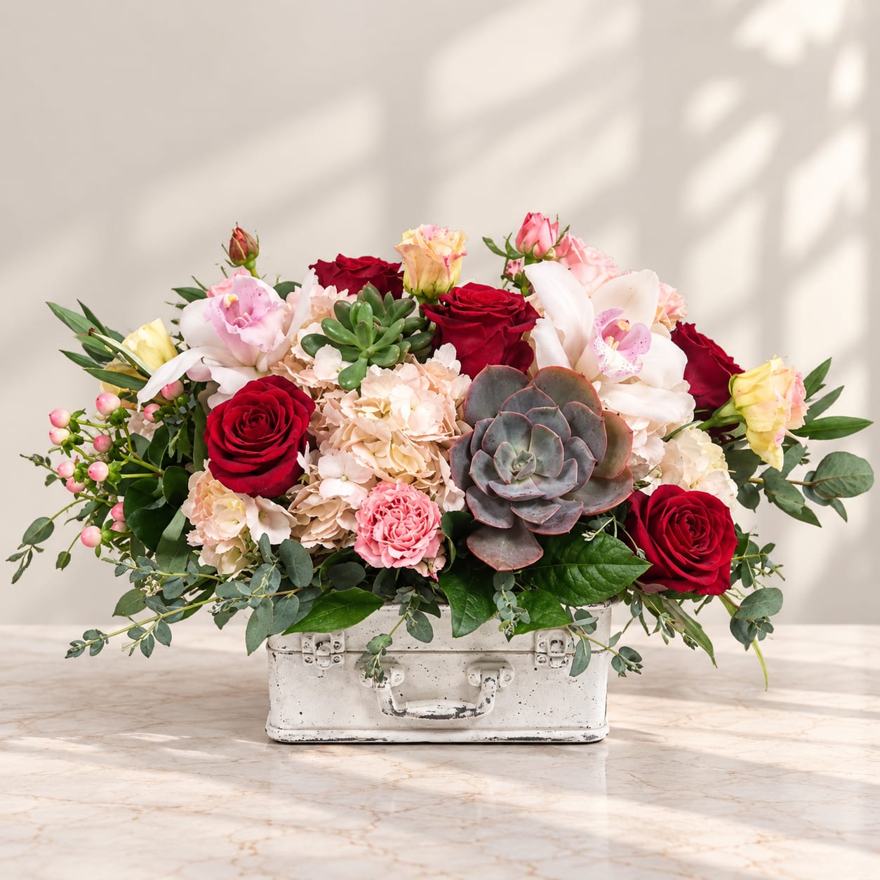 Mixed bouquet of roses, orchids, carnations, and succulents in a white container