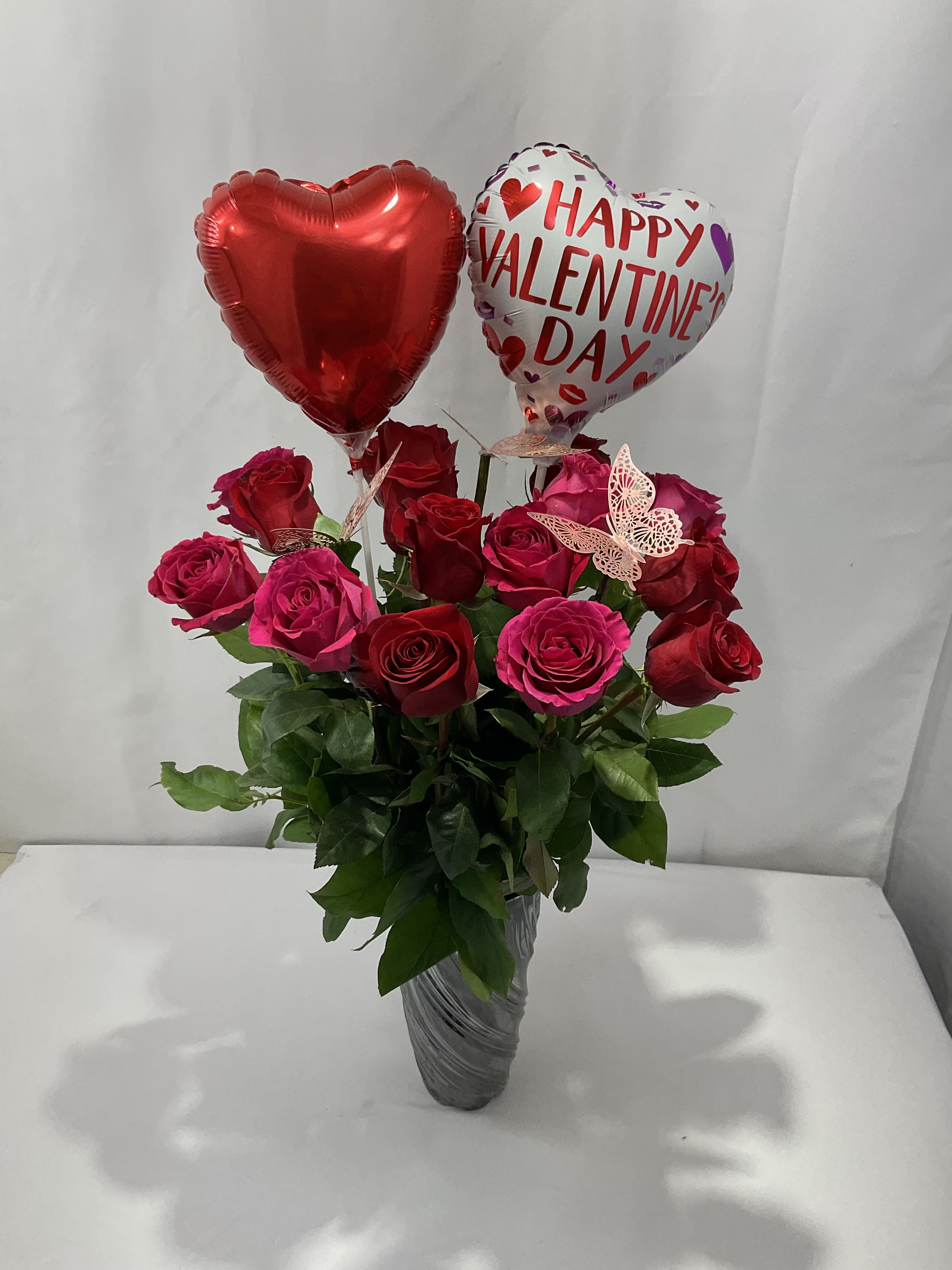 Red and pink roses in a vase with two heart balloons