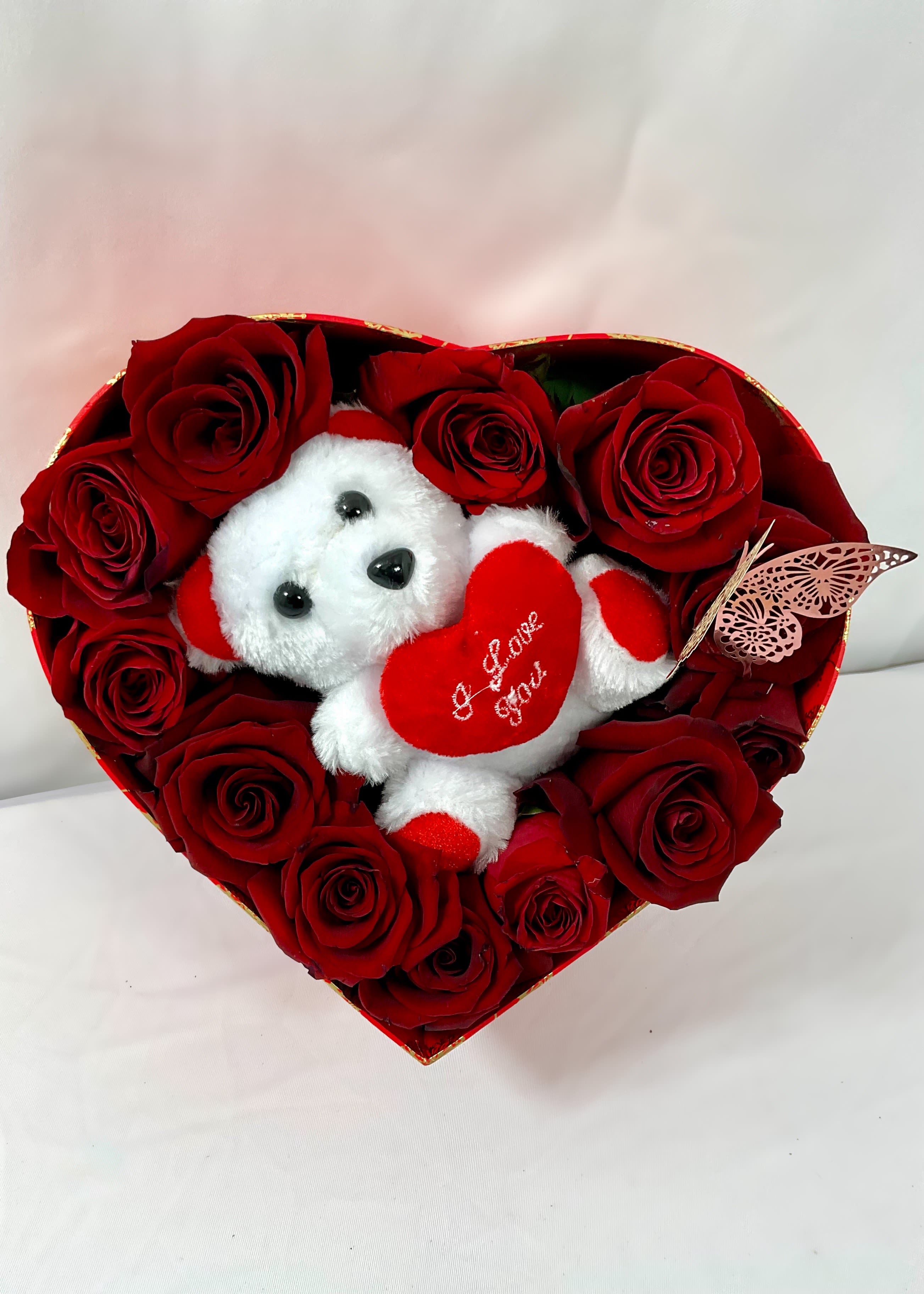 Heart-shaped box of red roses with a small teddy bear holding a heart
