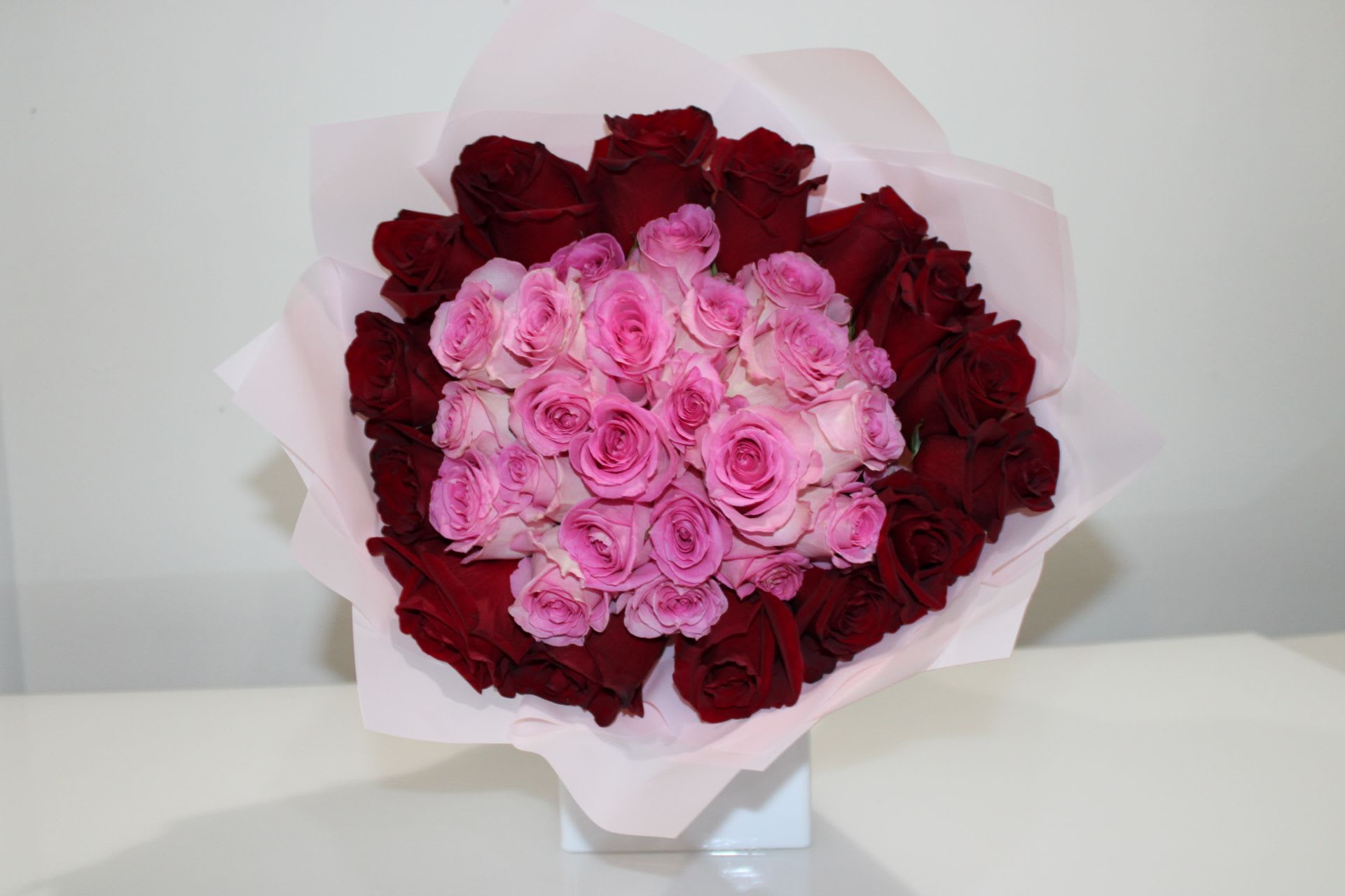 Bouquet of pink and red roses wrapped in pale pink paper