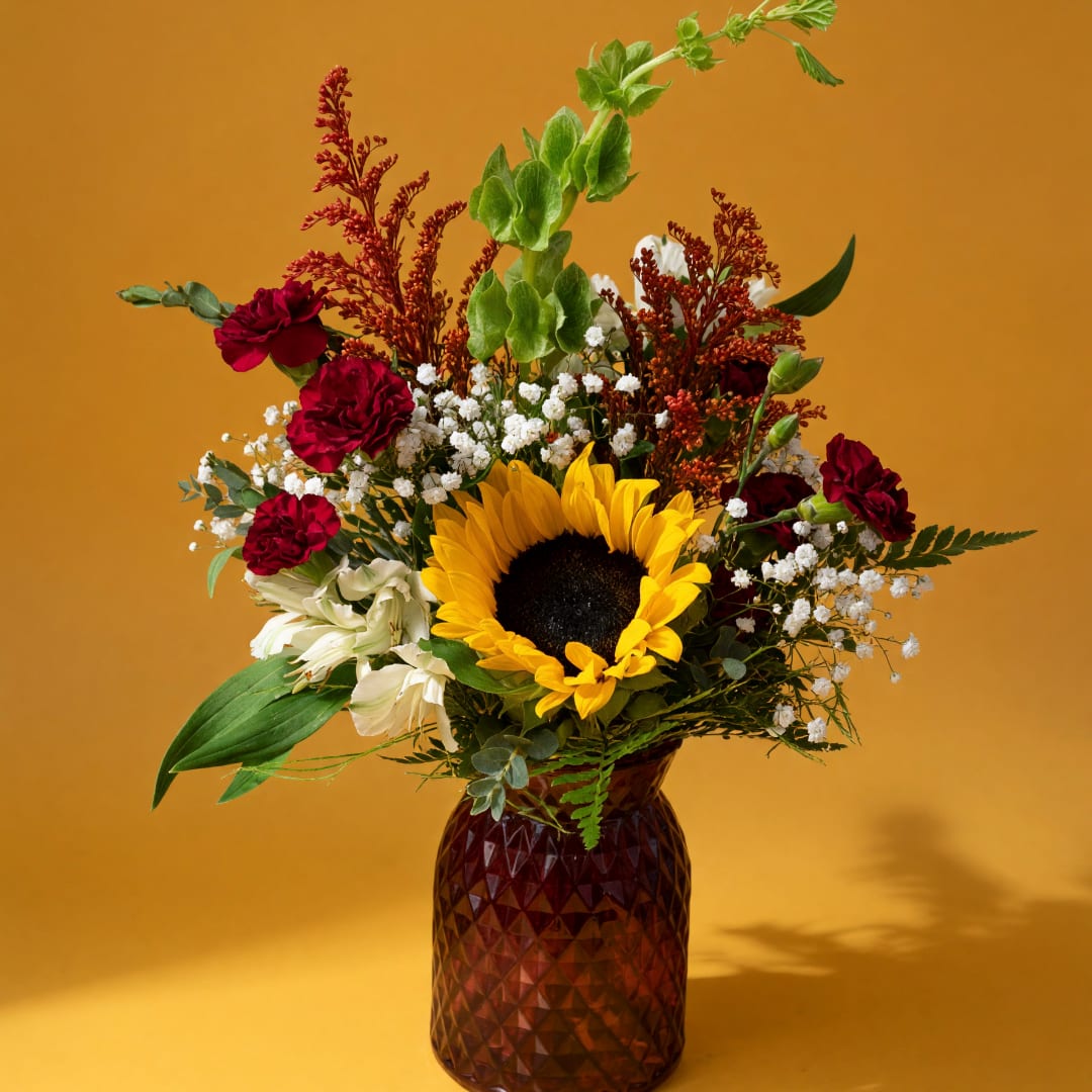 Sunflower and red flower arrangement in a textured amber vase