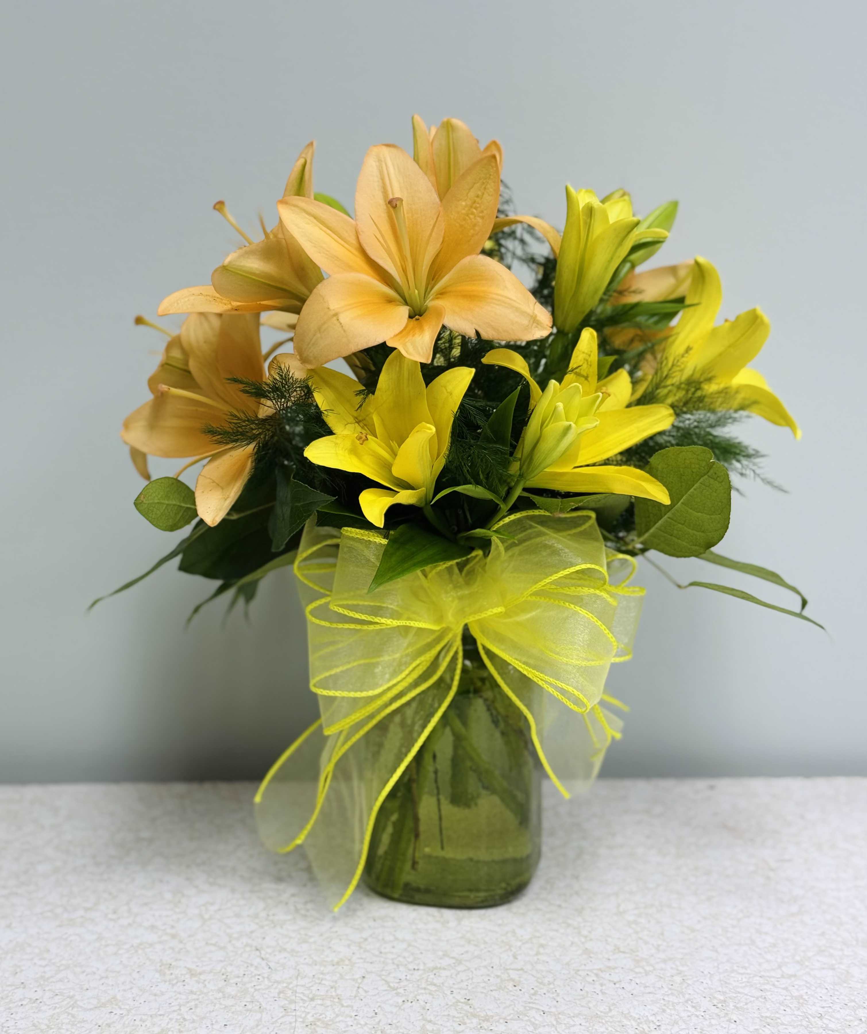 Yellow and peach lilies arranged in a glass vase with a ribbon bow.