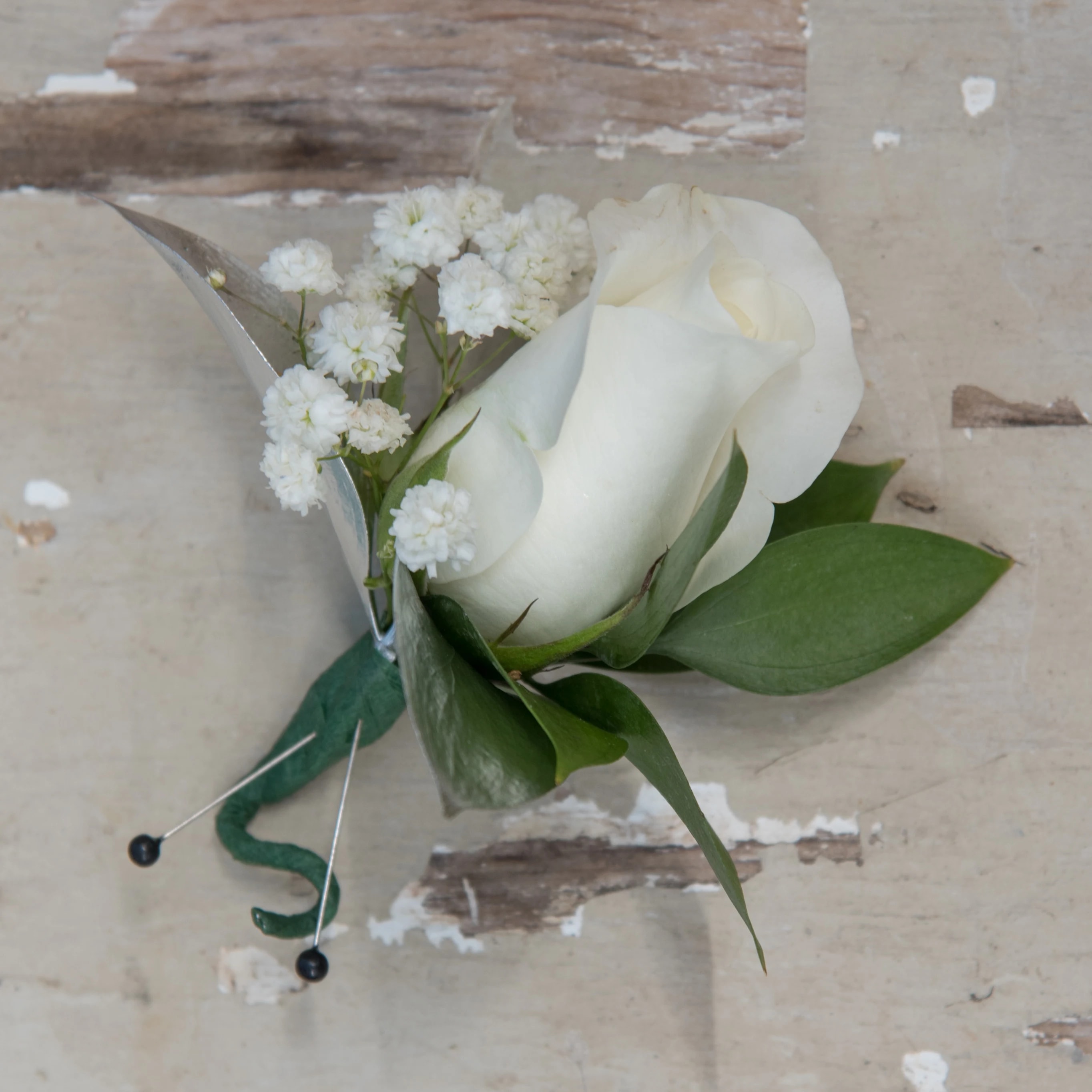 White rose boutonniere with baby's breath and green leaves
