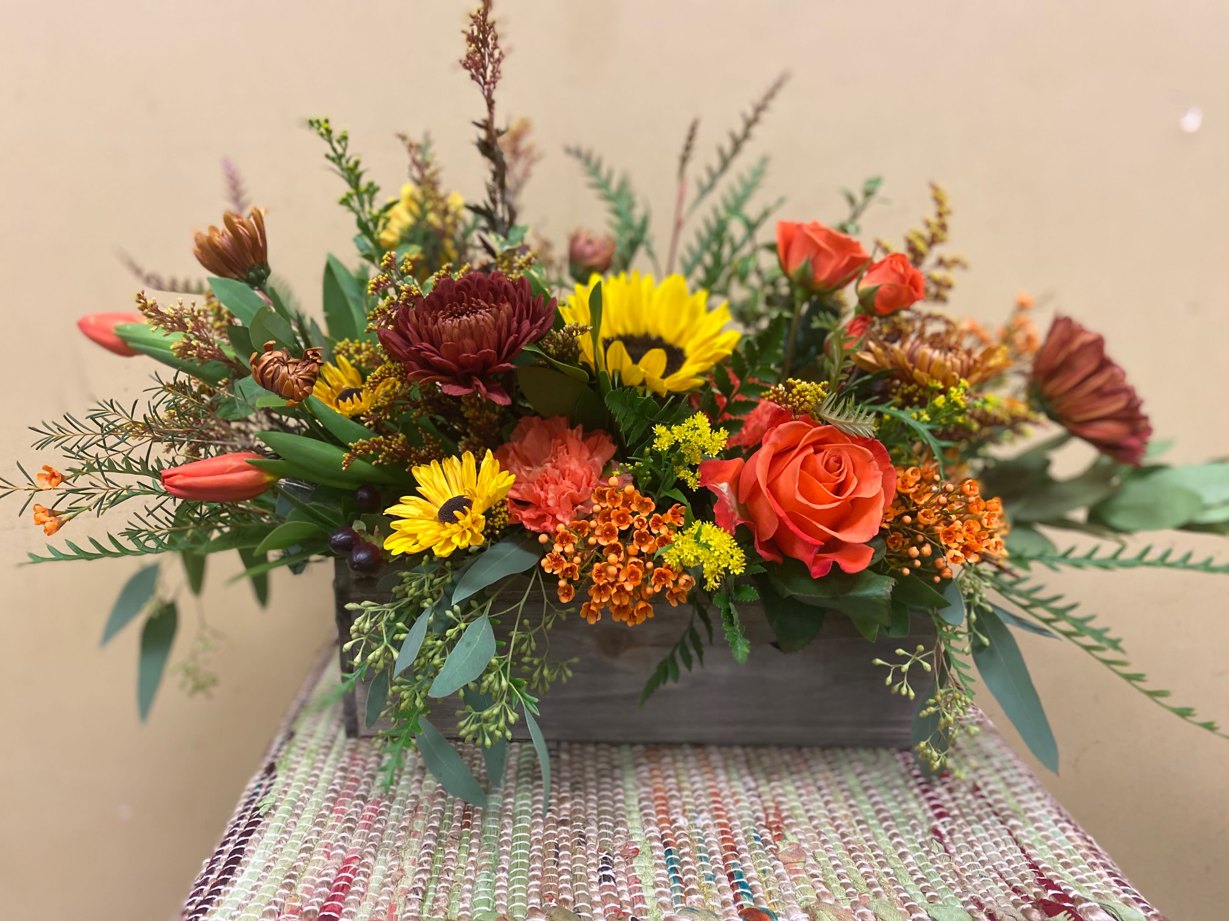 Mixed floral arrangement in a rectangular wooden container with orange and yellow blooms
