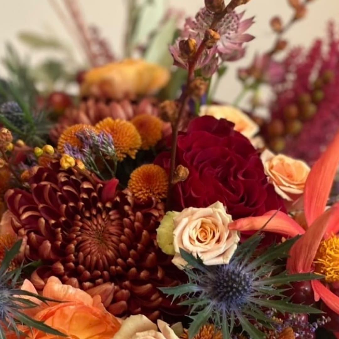 Autumn bouquet with red and peach roses, orange mums, and thistle-like blooms