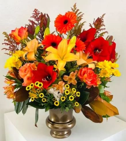 Bright mixed flower arrangement in a gold vase with red, orange, and yellow blooms