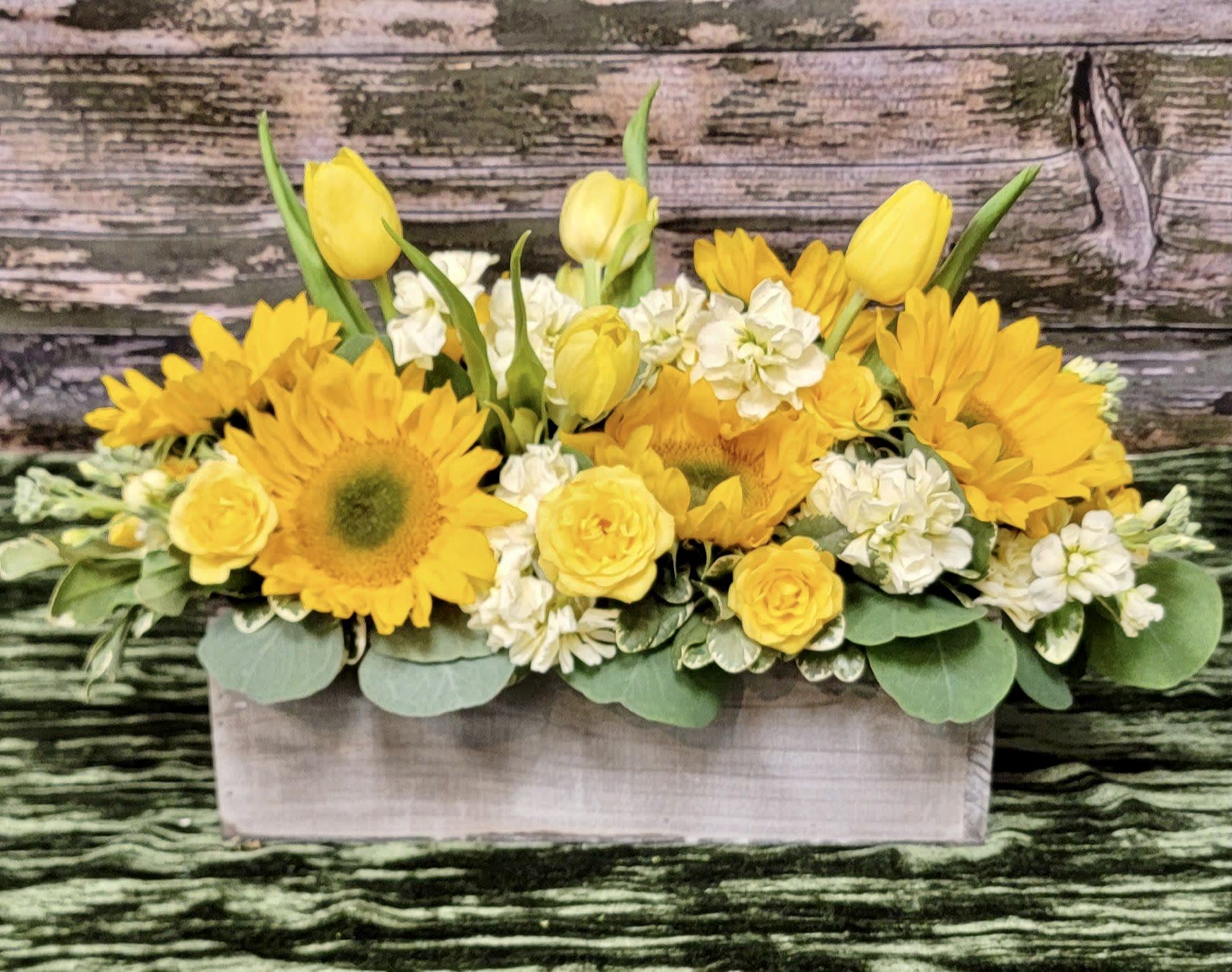 Yellow tulips, sunflowers, and white flowers in a rectangular wooden box