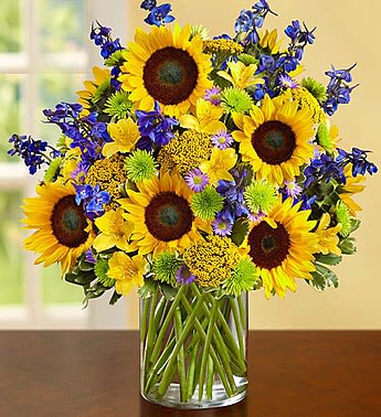 Sunflower bouquet in a clear glass vase with blue and green accent flowers
