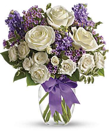 Teleflora's Enchanted Cottage - This magical bouquet will be at home in a cottage, a condo, a studio or an estate. It's so pretty it will be appreciated by all those lucky enough to receive it. Enchant someone today! White roses and spray roses, lavender stock and waxflower, all perfectly arranged in a clear glass vase that's wrapped with purple ribbon. Orientation: One-Sided