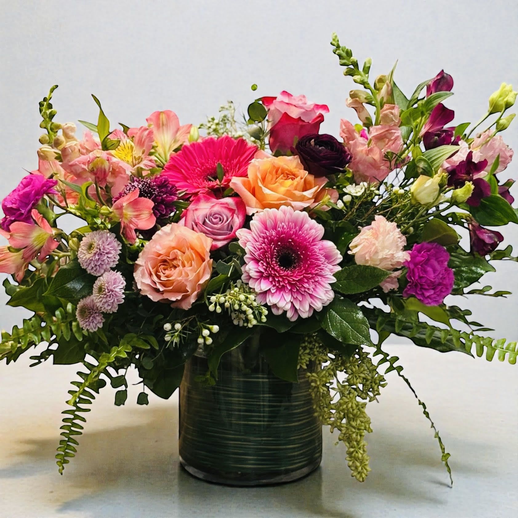 Mixed bouquet of pink, peach, and purple flowers in a dark vase