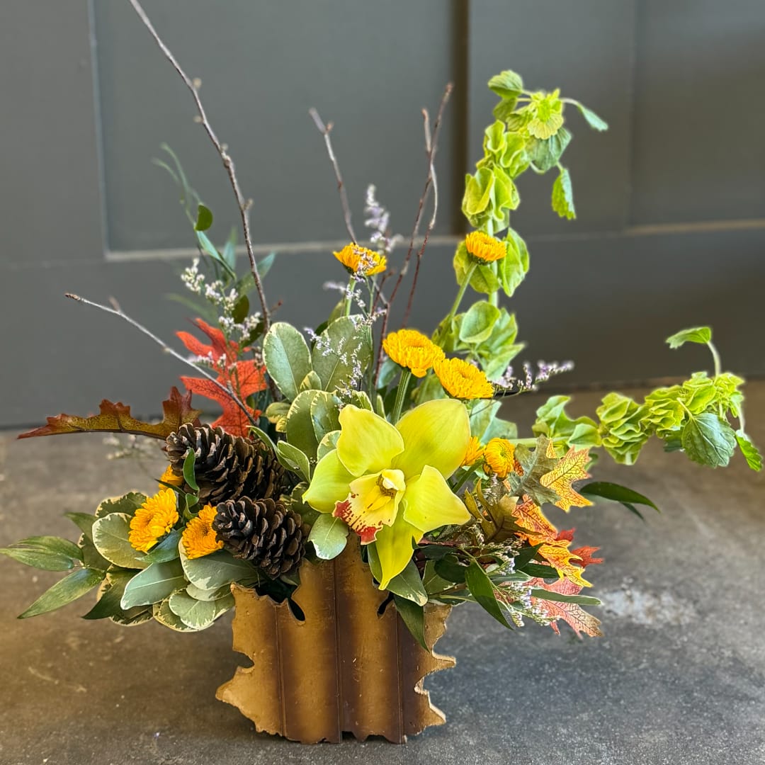 Autumn floral arrangement with yellow orchid, mums, pinecones, and fall leaves in a rustic container