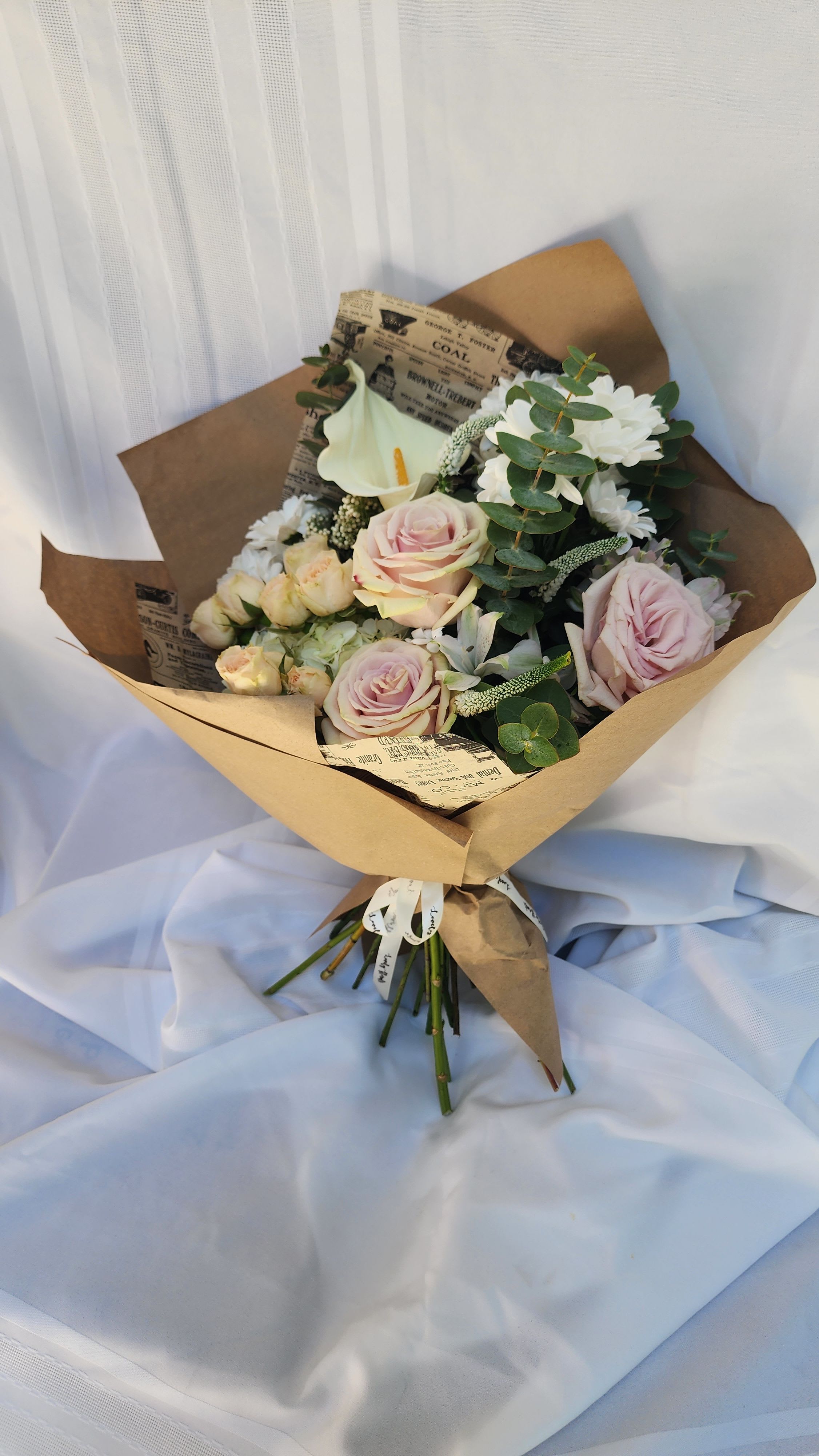 Bouquet of pale pink roses and white flowers wrapped in brown paper