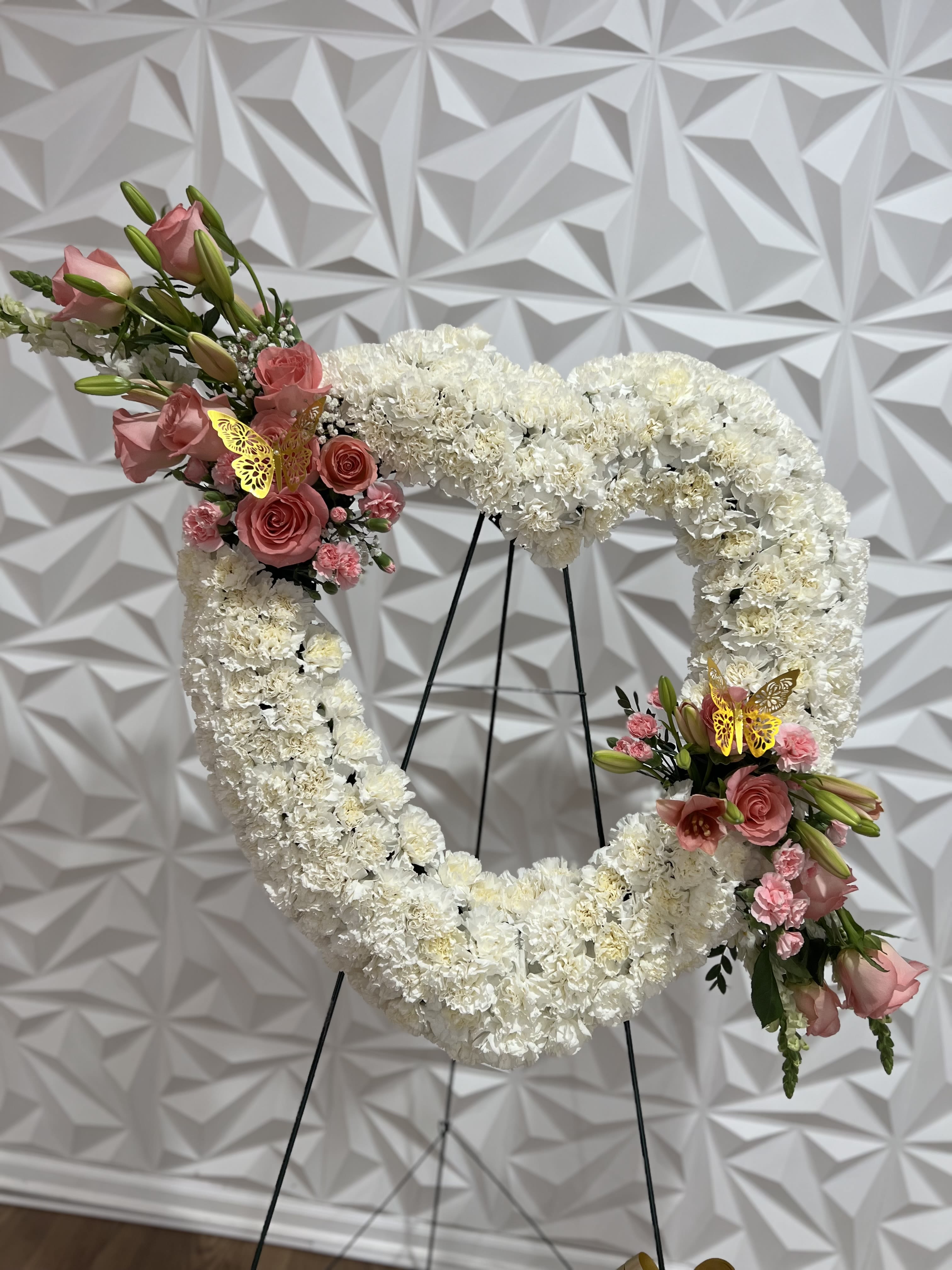 Heart-shaped white floral wreath with pink rose accents on a stand
