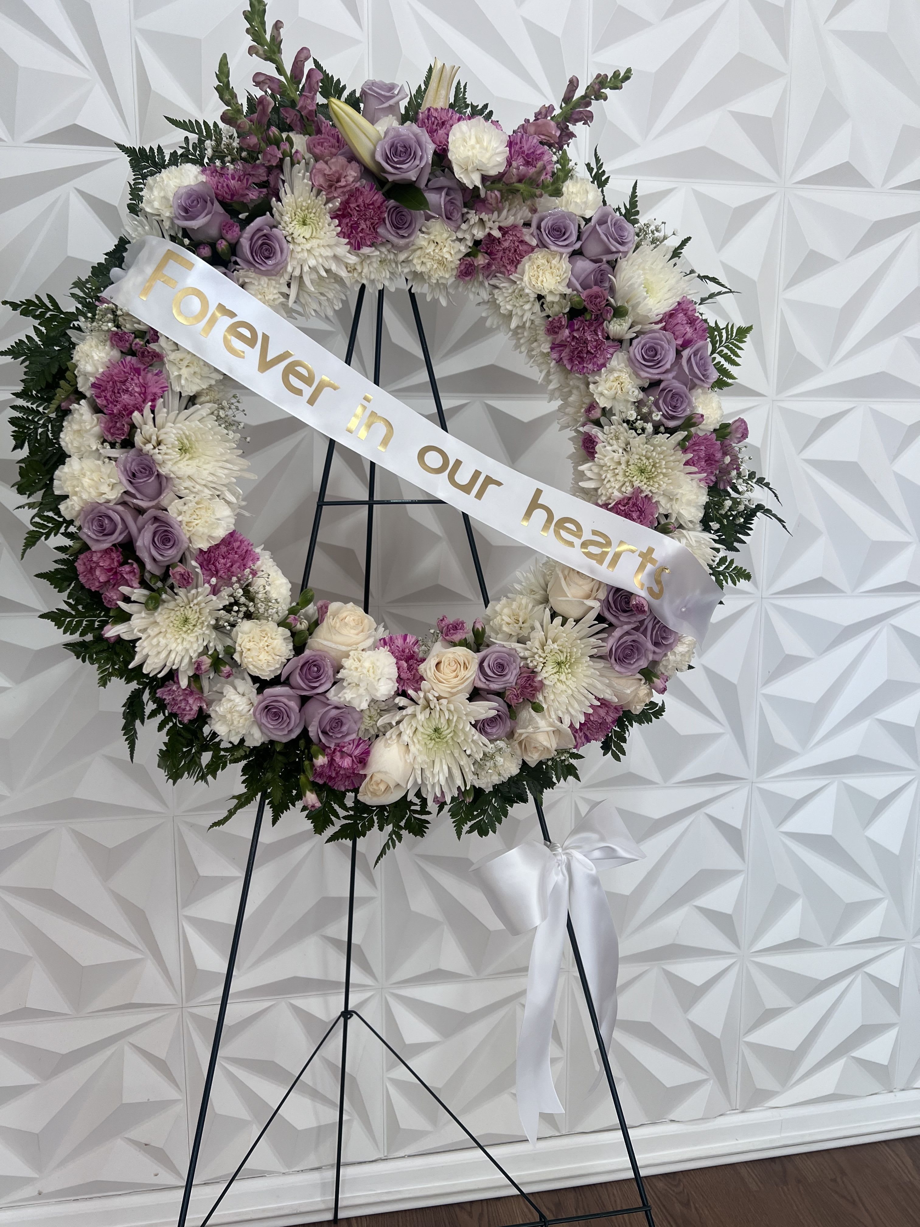 Floral memorial wreath on an easel with a ribbon reading "Forever in our hearts"