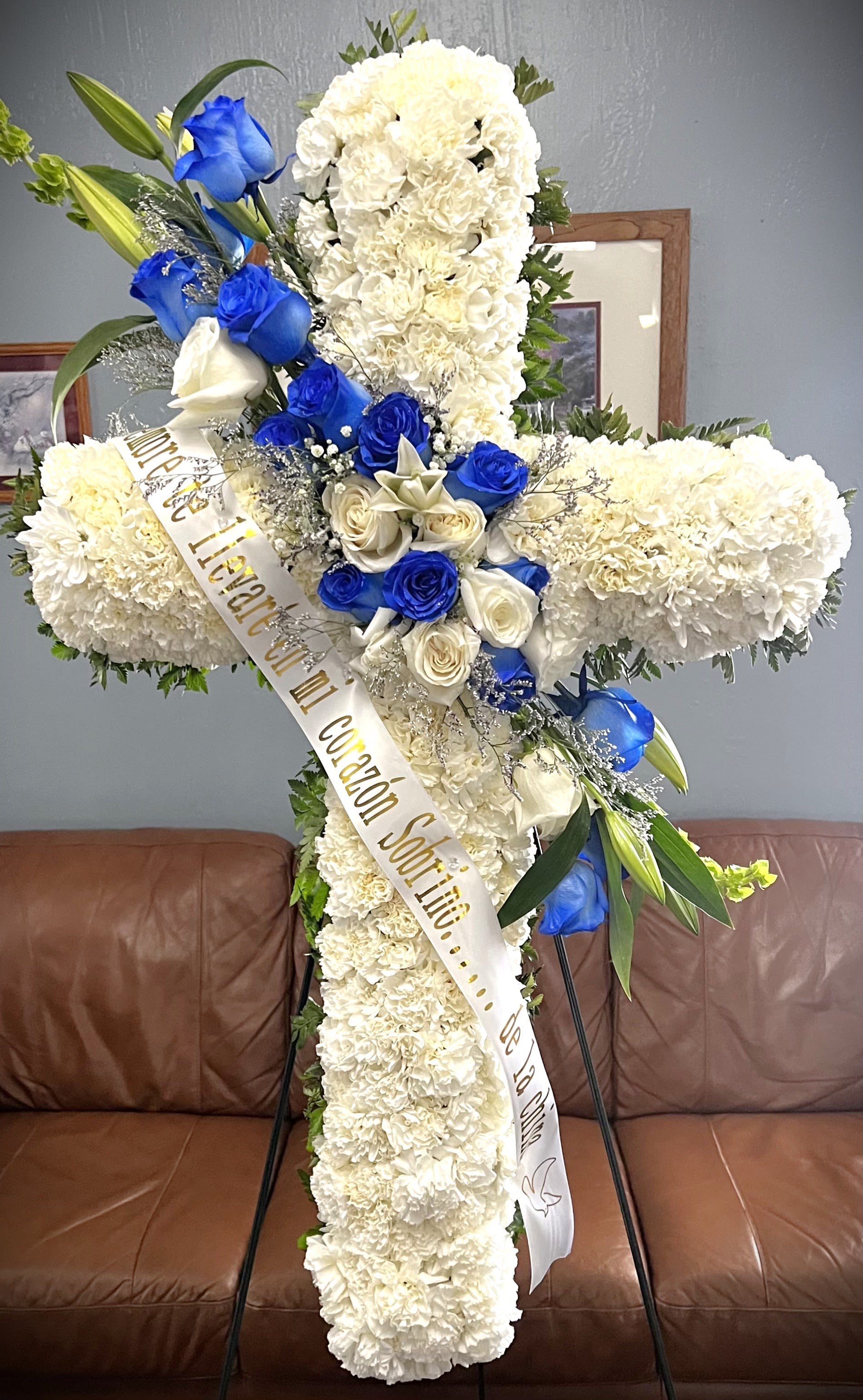 White floral funeral cross with blue and white roses and a memorial ribbon