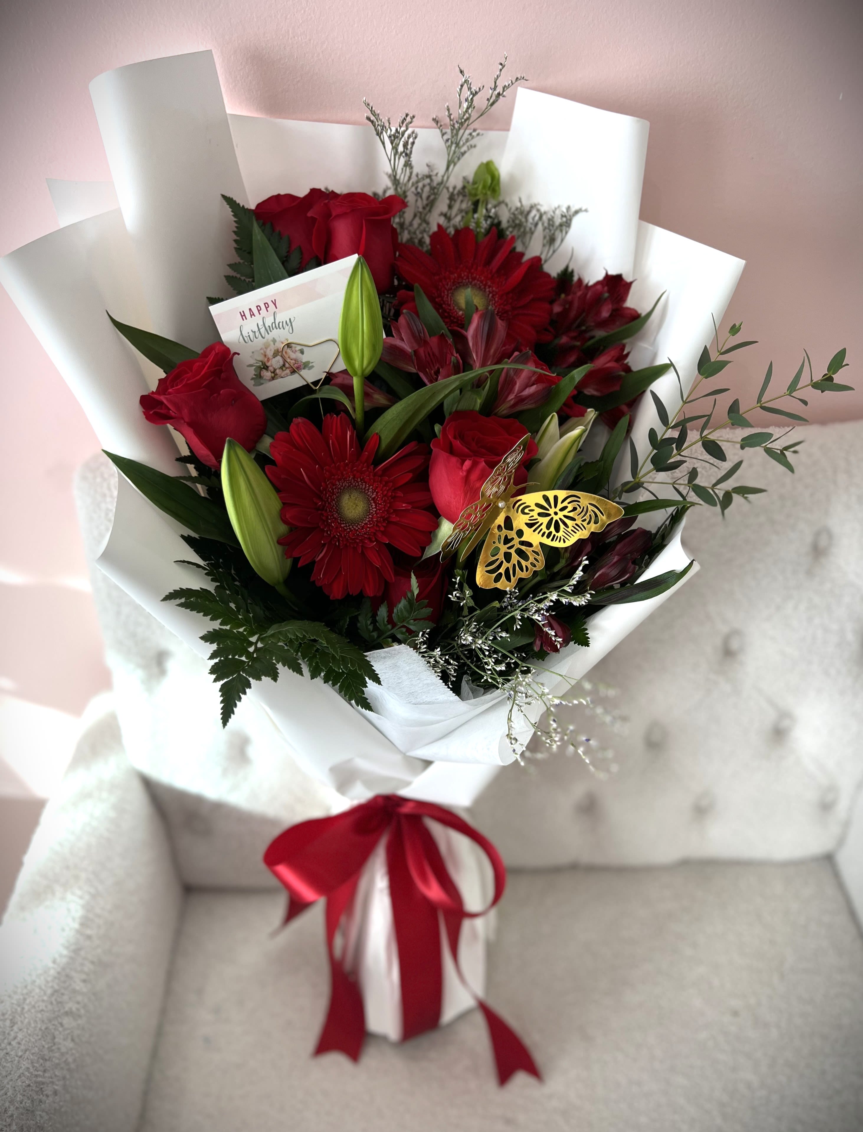 Red roses and gerbera daisies in white wrap with a birthday card