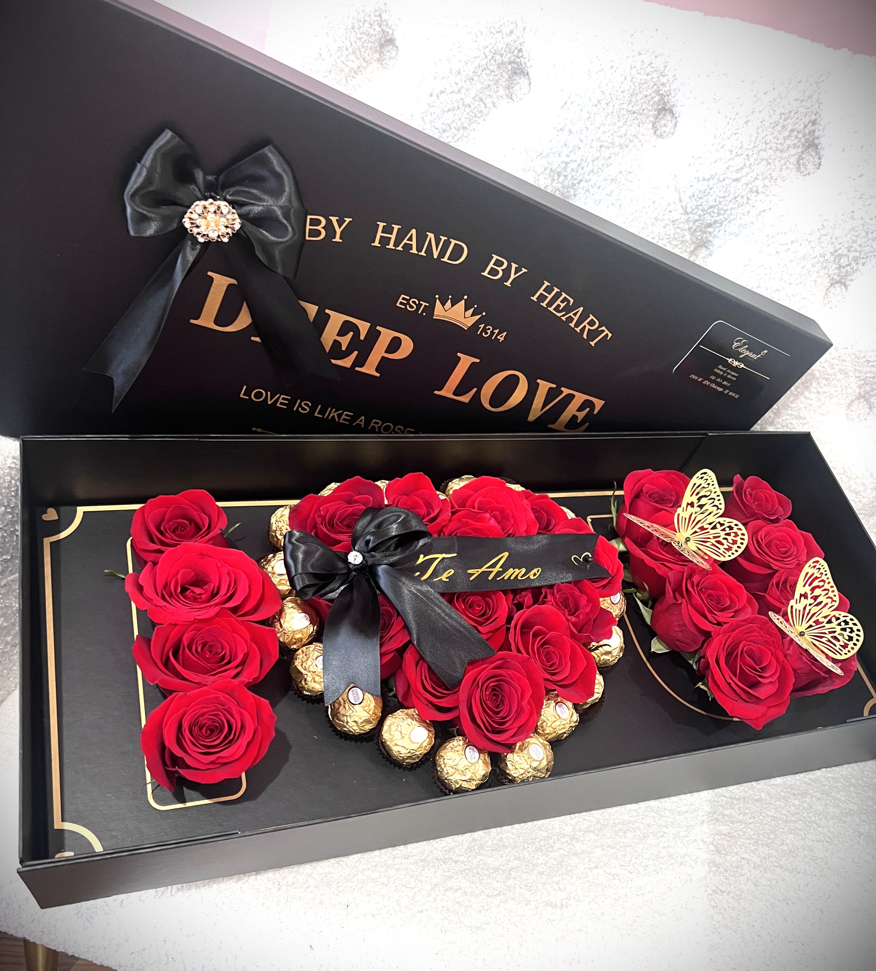 Red roses arranged in a black gift box with gold chocolates and ribbon
