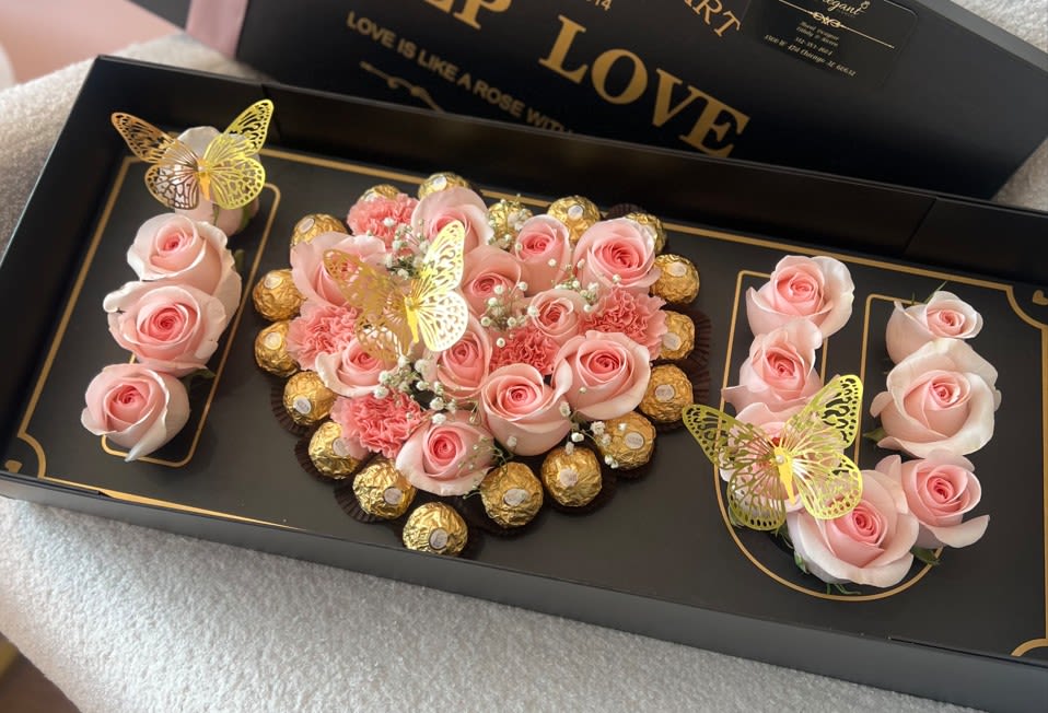 Pink roses and chocolates arranged in a black gift box with butterfly decorations.
