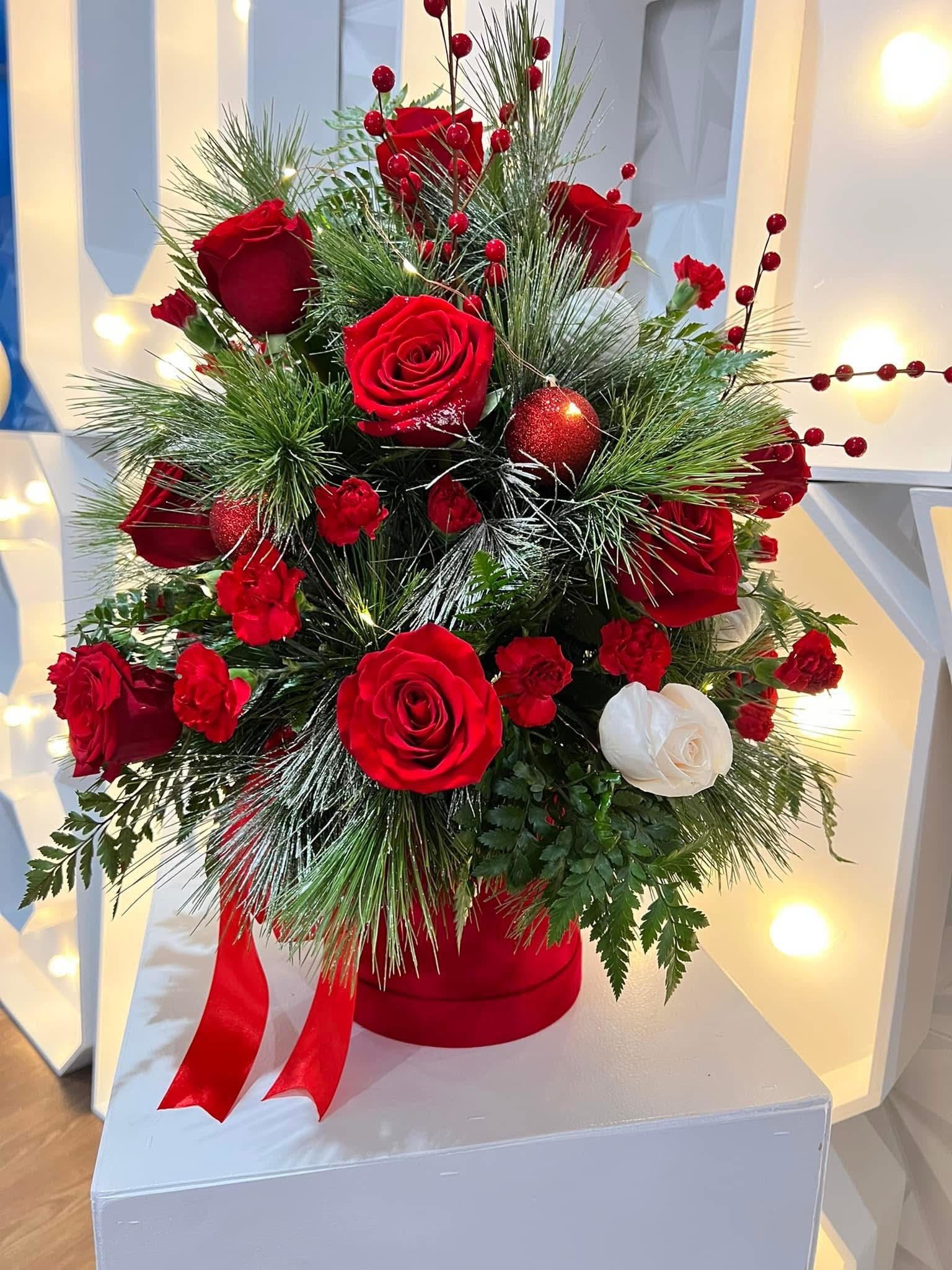 Red and white roses arranged with pine and berries in a red hatbox