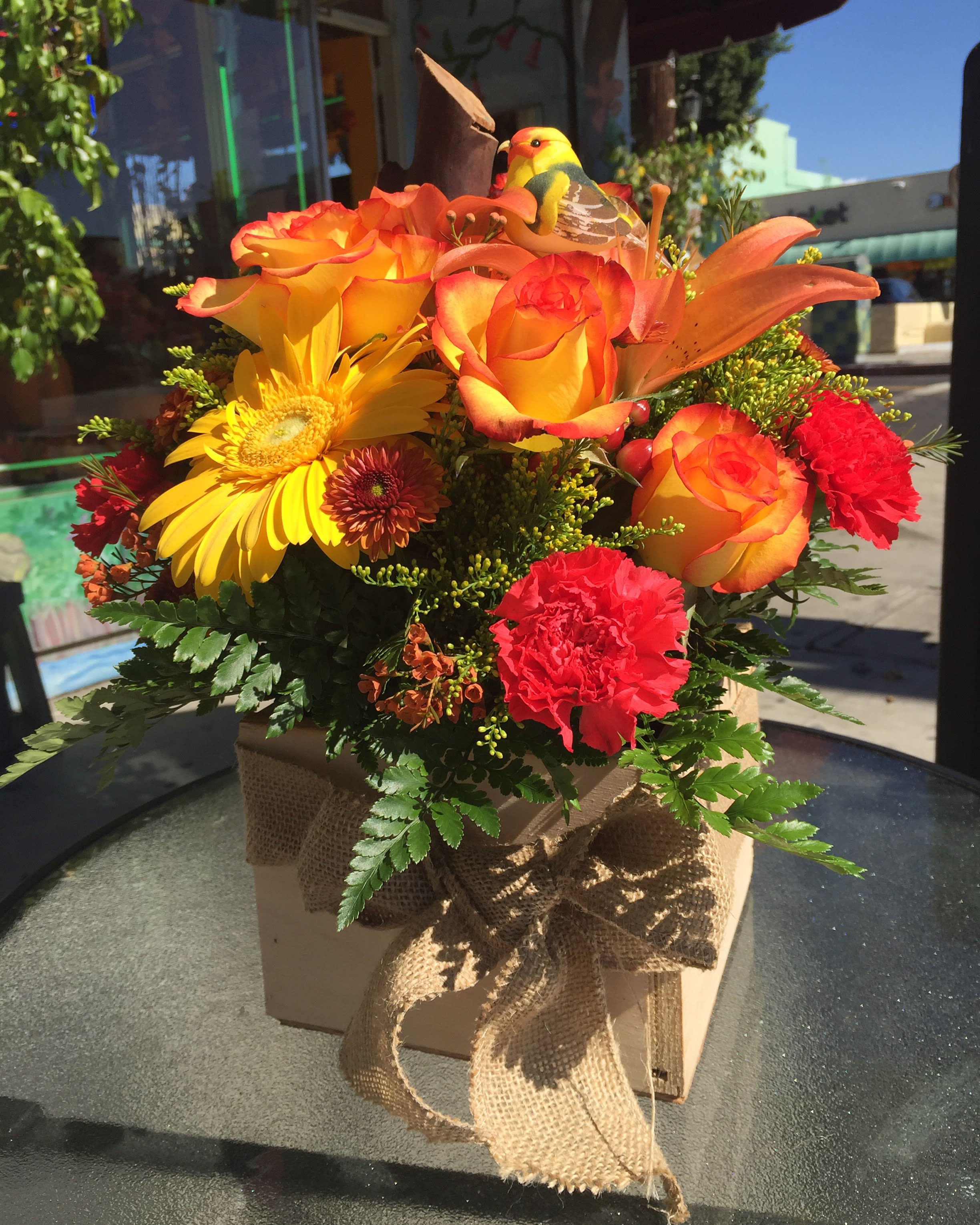 Orange and yellow floral arrangement in a burlap-tied box with a bird decoration
