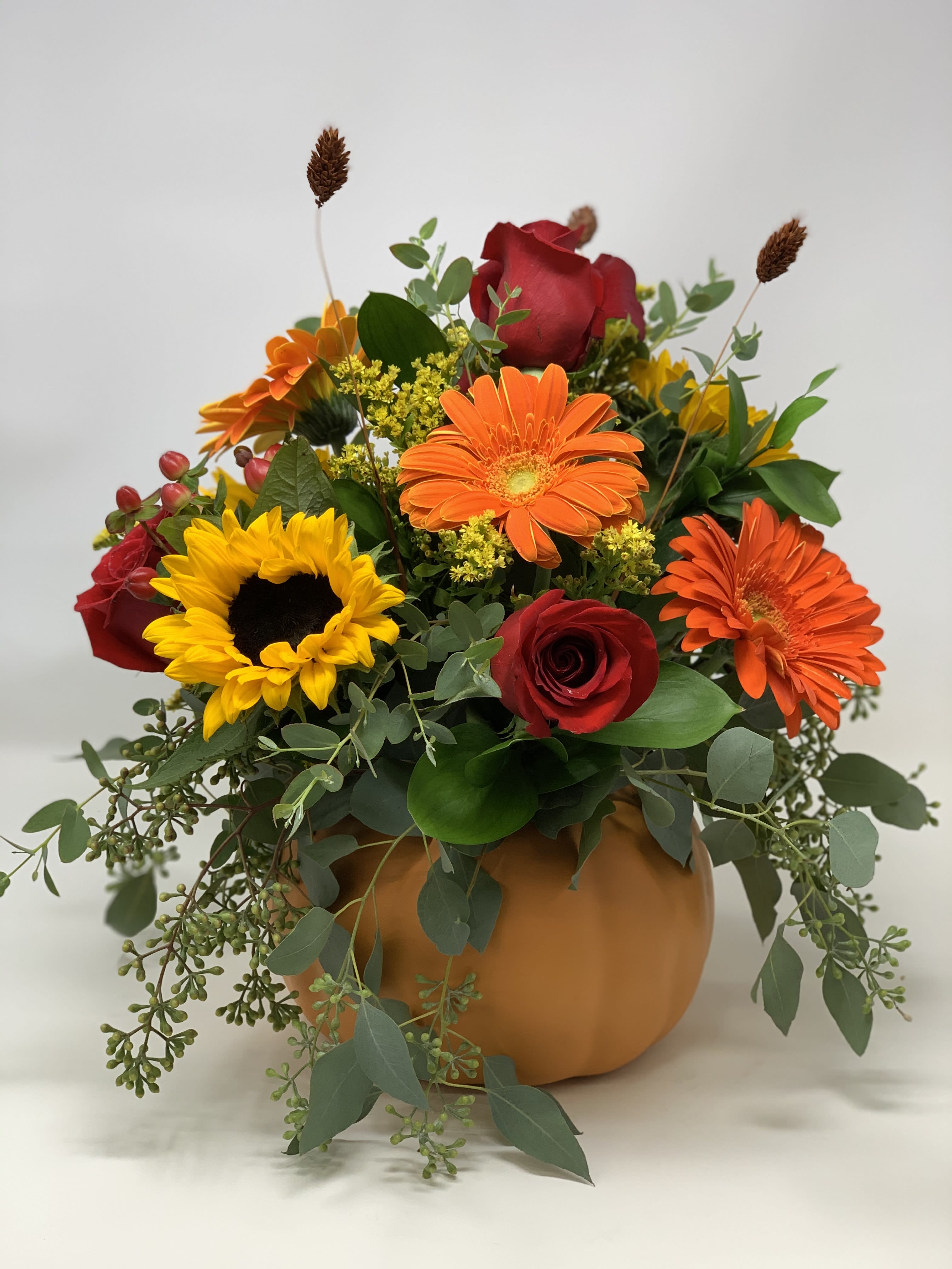 Pumpkin-shaped vase with red roses, orange gerberas, and a sunflower