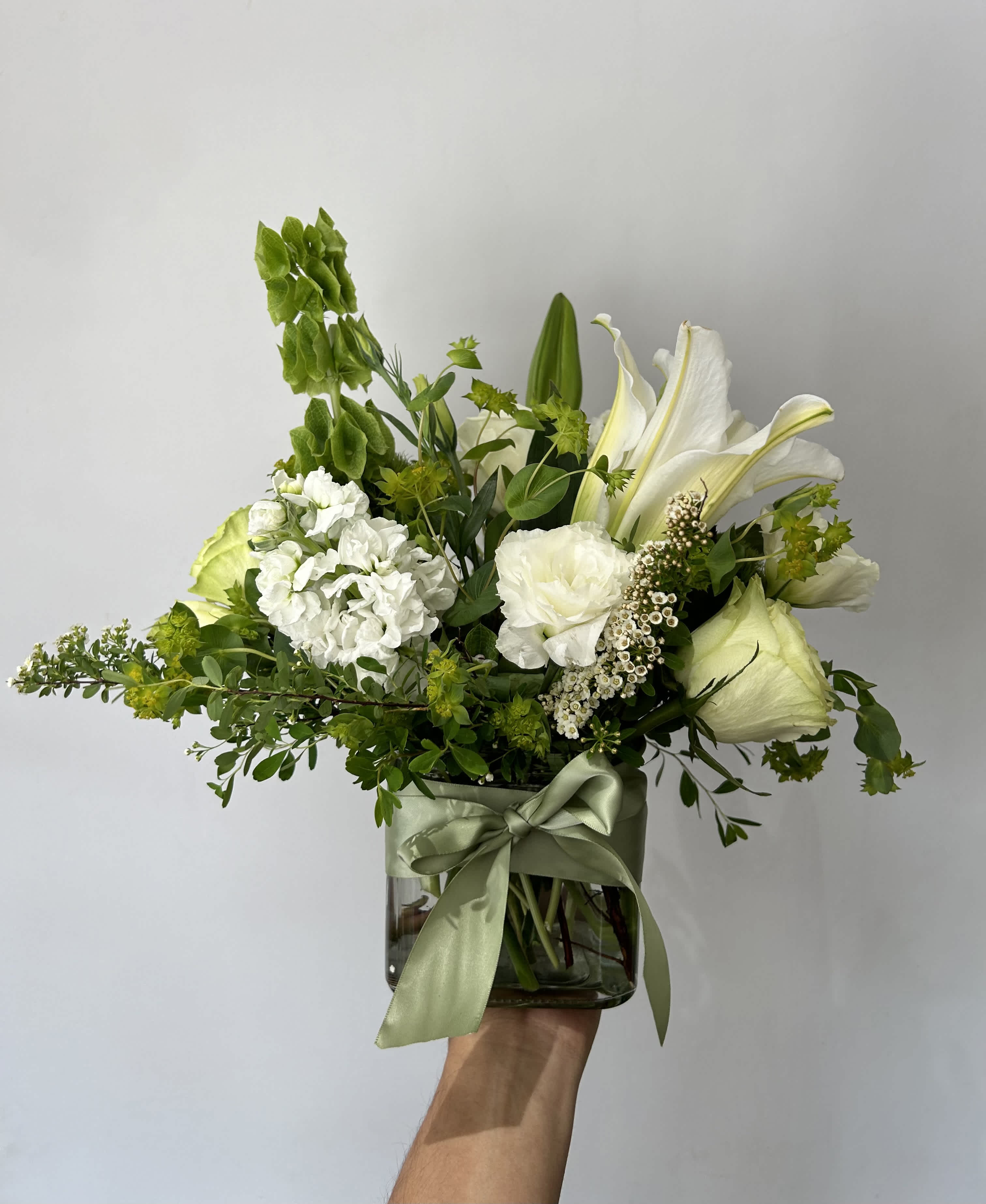 White floral arrangement in a glass vase with a green ribbon