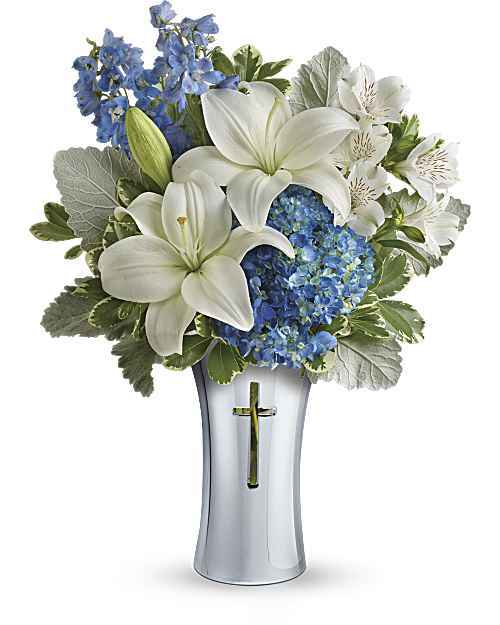 White lilies and blue flowers arranged in a silver vase with a cross