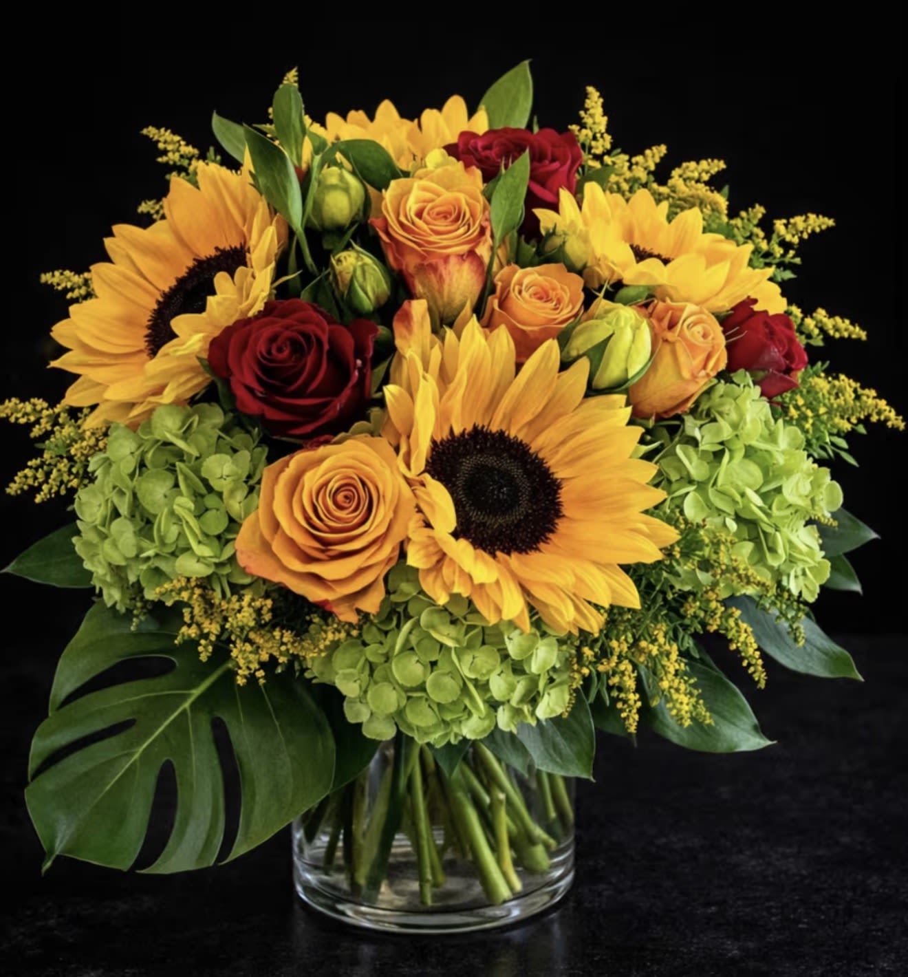Bouquet of sunflowers, roses, and hydrangeas in a glass vase