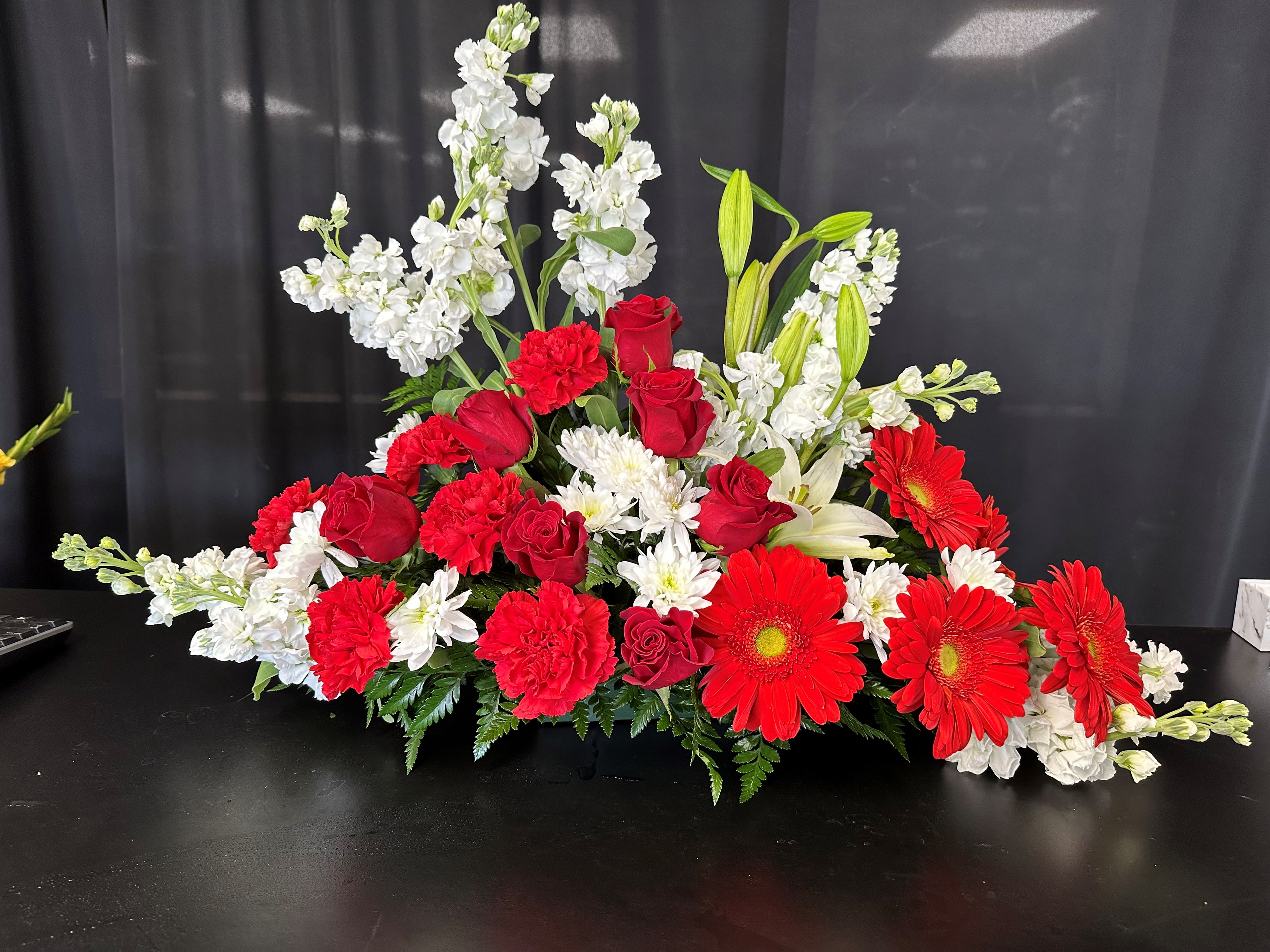 Crimson &amp; White  - Embrace the beauty of peace and love with our Crimson &amp; White arrangement, a heartfelt tribute to the departed. Vibrant red roses, carnations, and gerbera daisies stand out against the backdrop of white stock, Oriental lilies, and chrysanthemums, creating a striking contrast that symbolizes eternal remembrance. Enhanced with lush greens, this exquisite arrangement exudes grace and reverence, serving as a beautiful expression of love and respect for the departed.