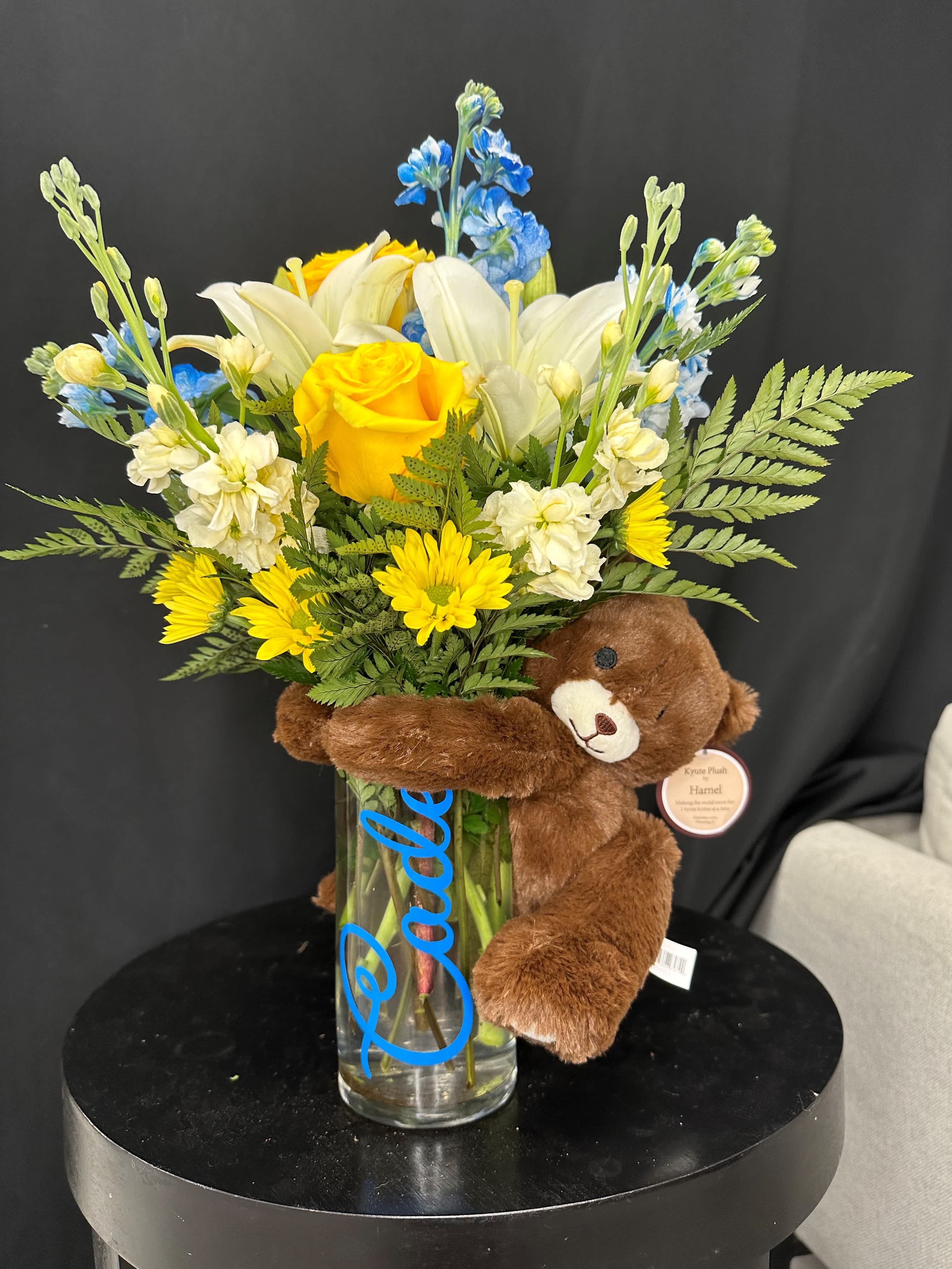 Bouquet of yellow and white flowers in a glass vase with a teddy bear