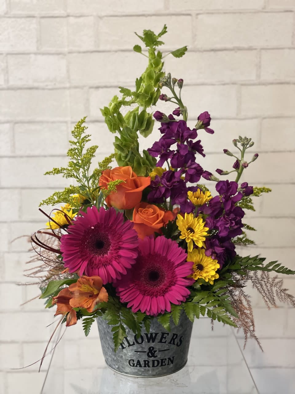 Mixed bouquet in a metal bucket with pink gerberas, orange roses, and purple blooms