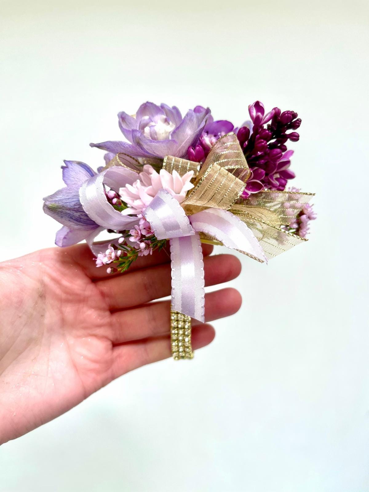 Small handheld corsage of purple and pink flowers with gold and lavender ribbon accents