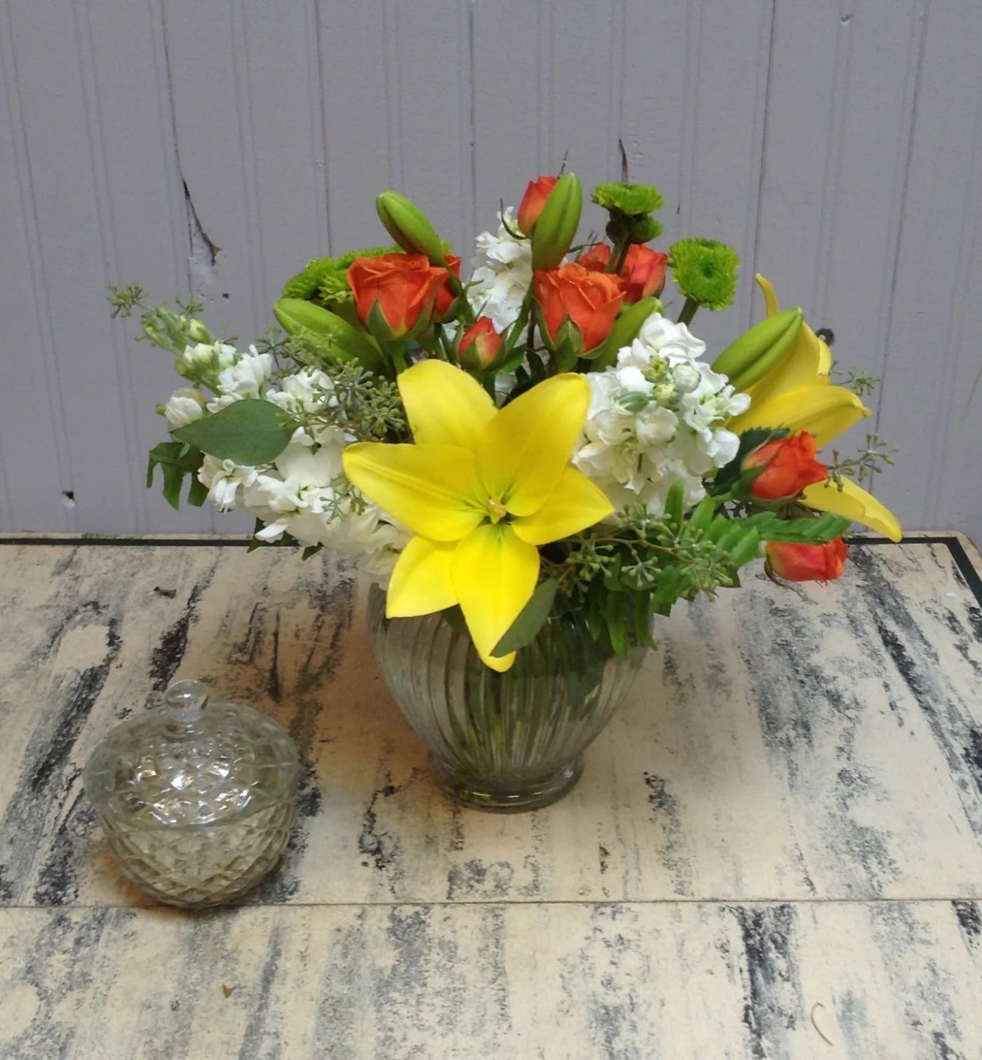 Bouquet of yellow lilies, orange roses, and white flowers in a glass vase