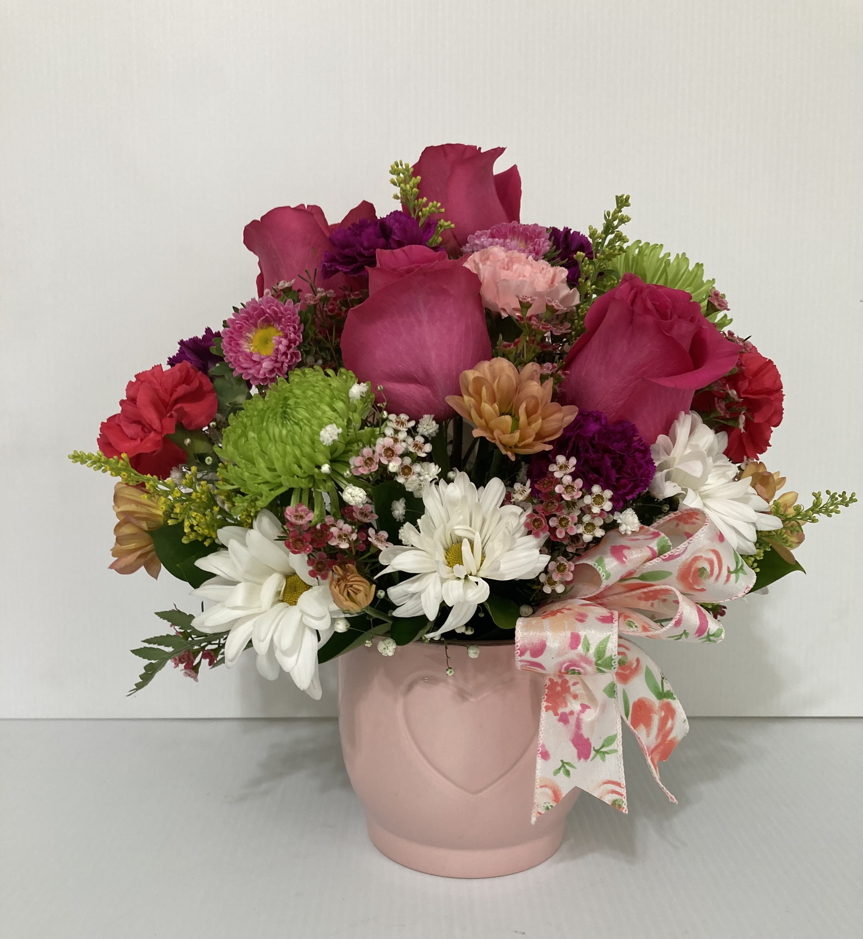 Mixed pink and white flowers in a pink vase with a floral ribbon
