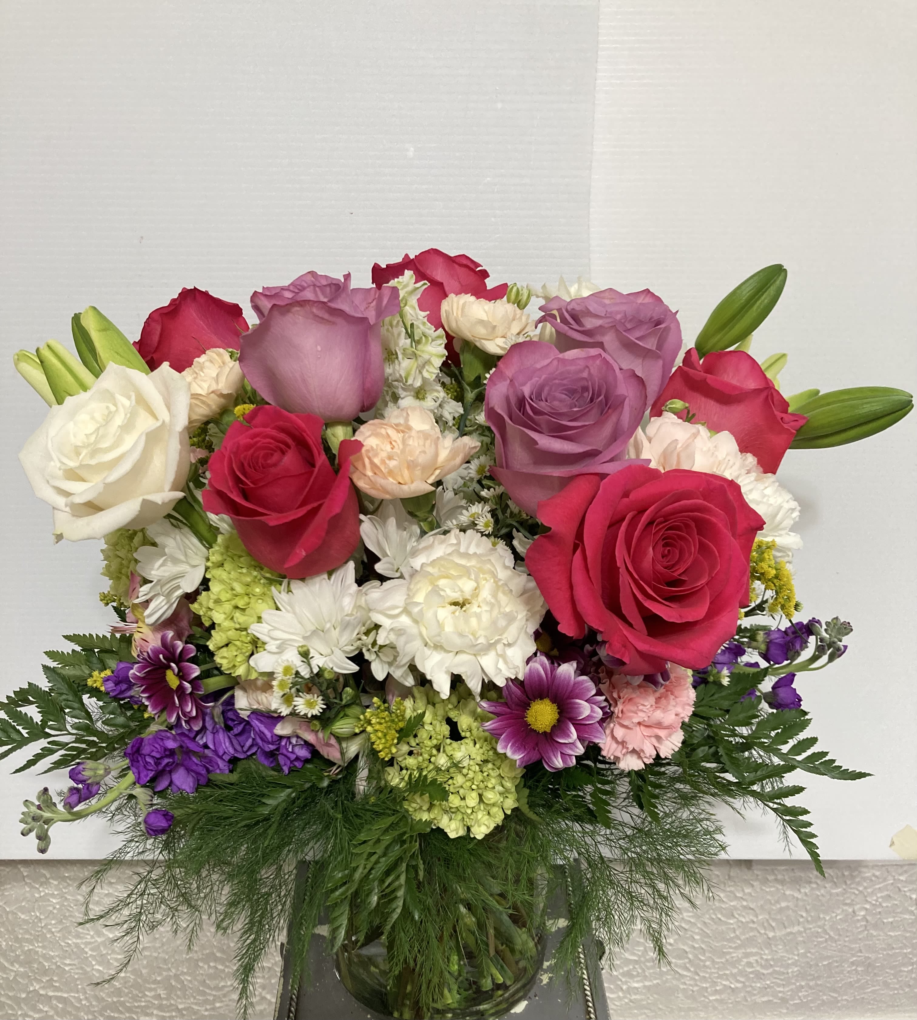 Mixed bouquet of roses, lilies, and daisies in a glass vase