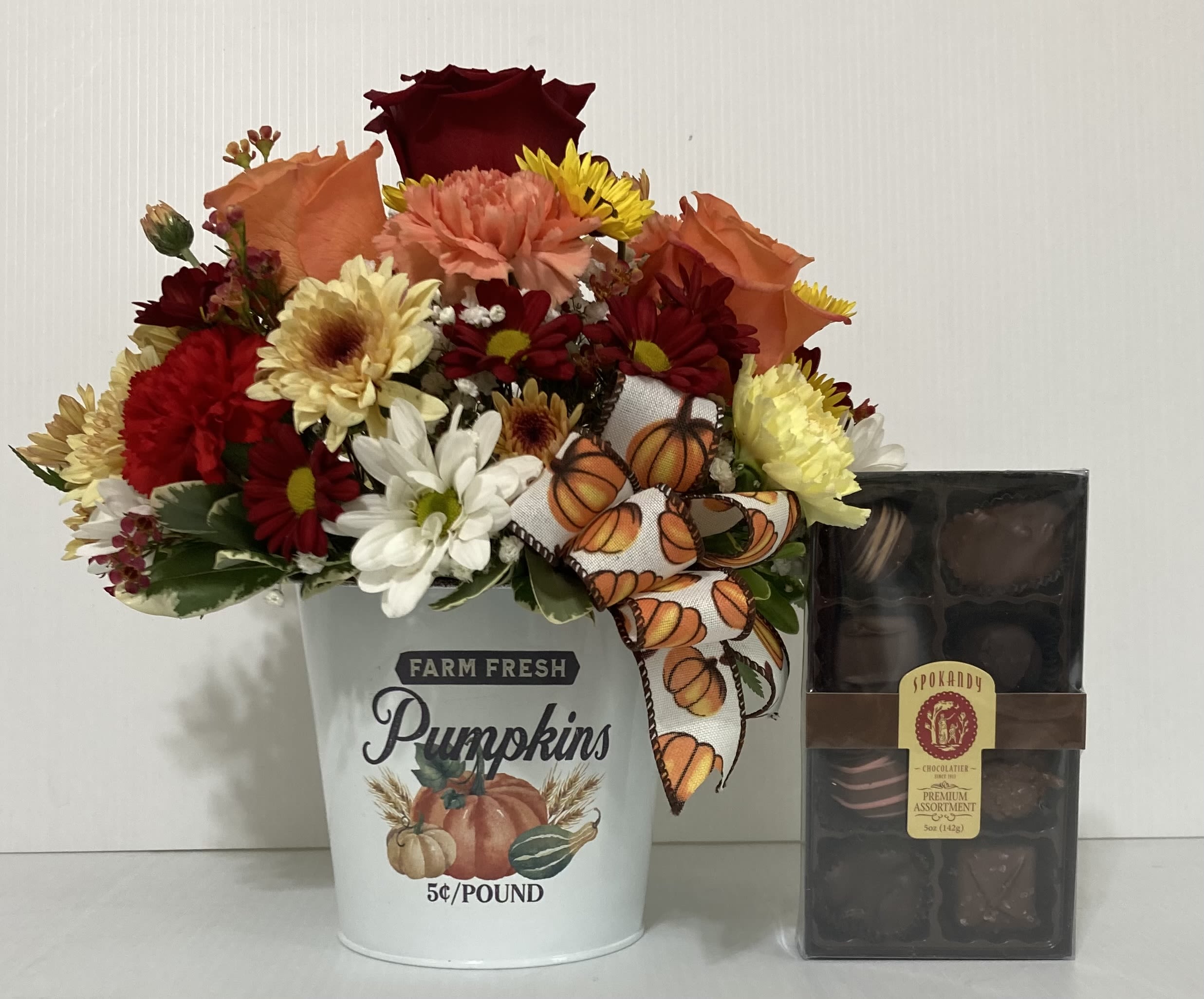 Fall flower arrangement in a pumpkin bucket beside a box of chocolates