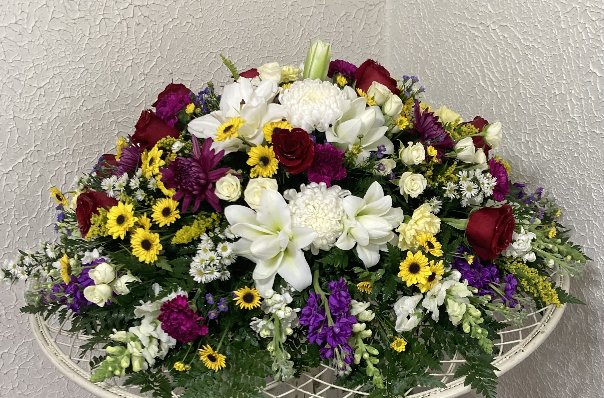 Large mixed floral arrangement with white lilies, red roses, and purple flowers