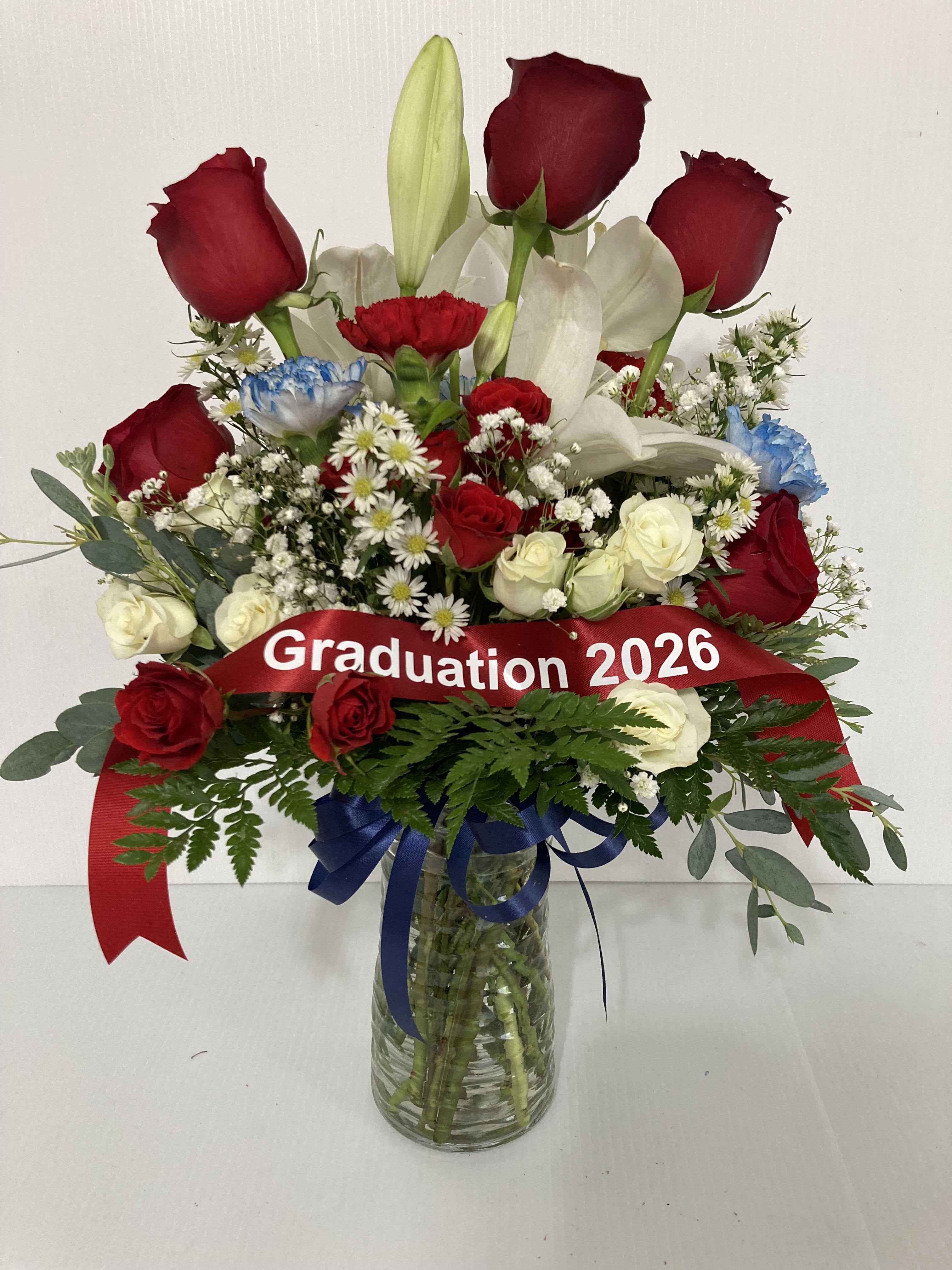 Red roses and white lilies in a glass vase with a graduation ribbon