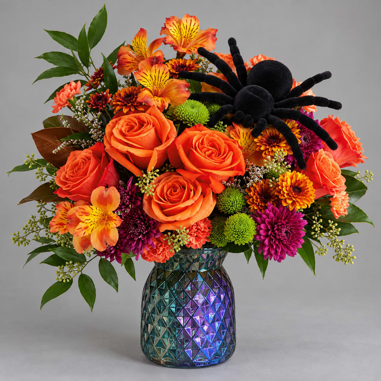 Orange and purple mixed bouquet in a faceted glass vase with a black spider decoration