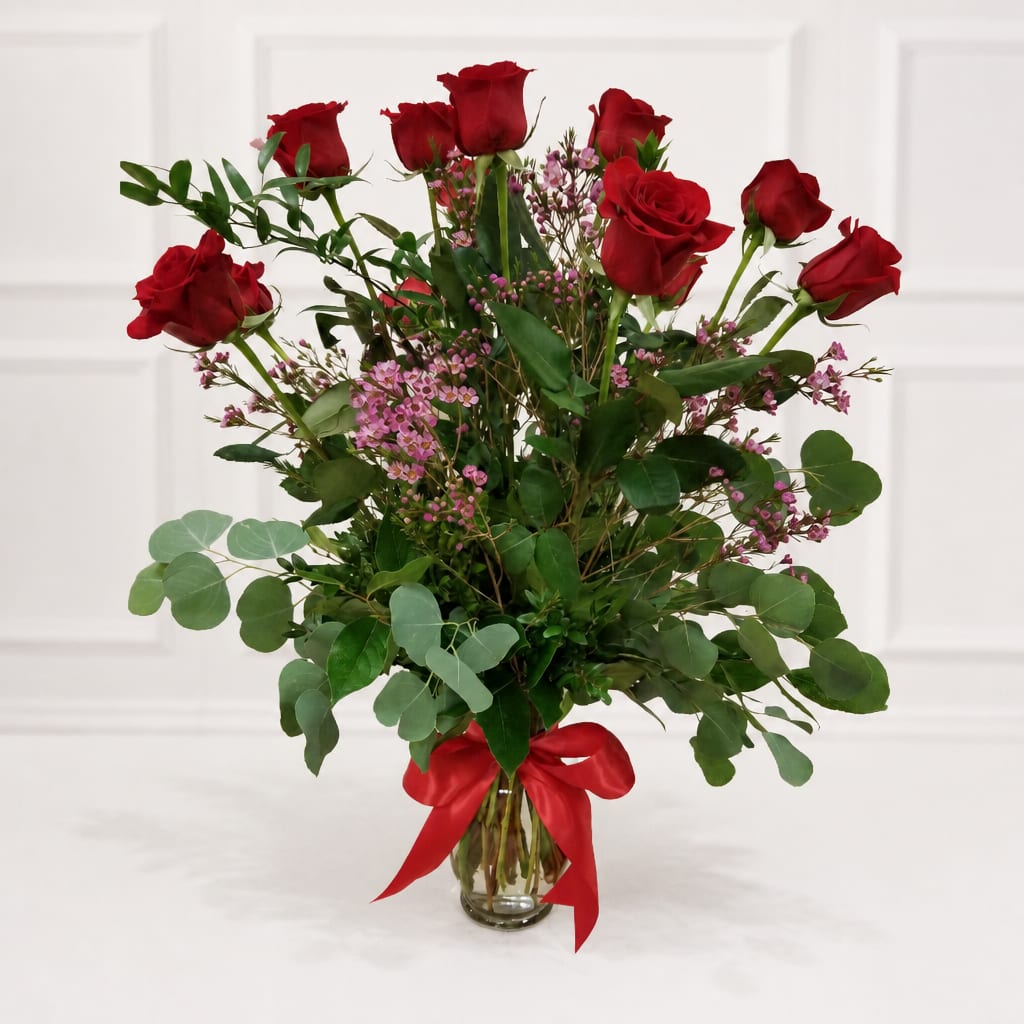 Red roses in a glass vase with pink filler flowers and a red ribbon