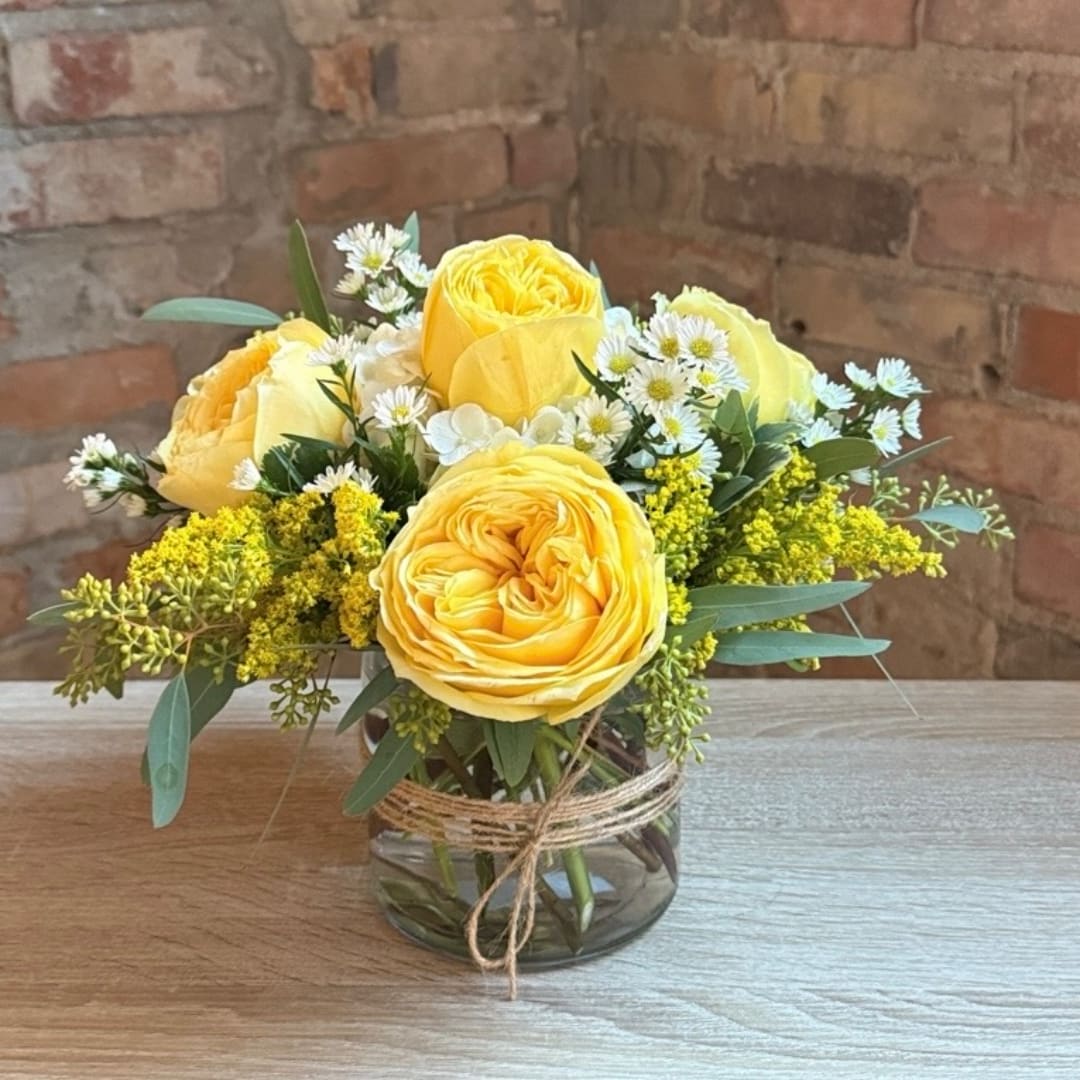 Yellow roses and small white daisies in a glass vase with twine