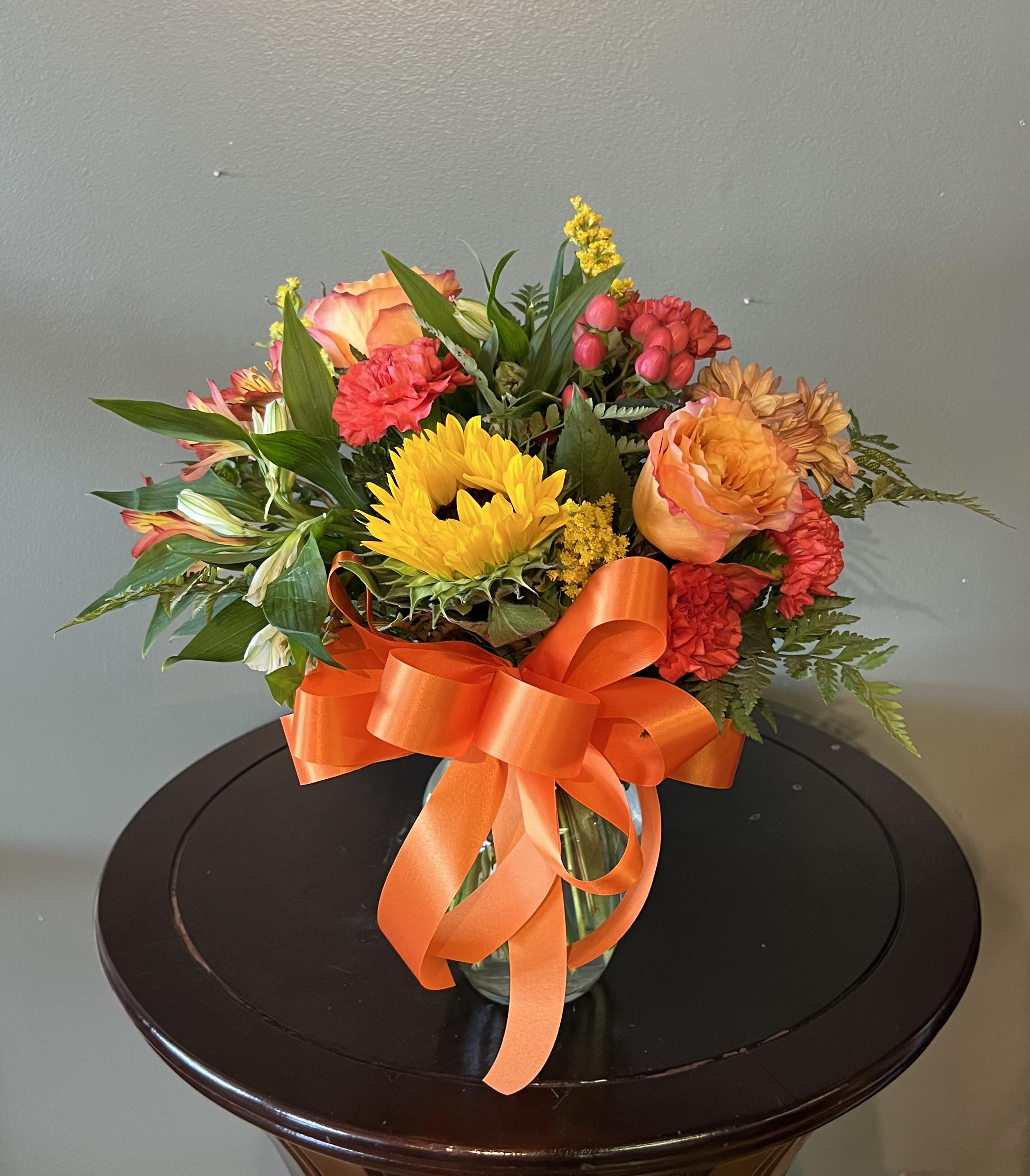 Sunny Harvest Garden - This fresh and festive bouquet will fill their home with the sights and scents of fall. Stunning sunflowers and other fall blooms explode out of a modern cinched glass vase. Treat someone special to a unique and bold arrangement. Flowers may change depending on product and flower availability.   