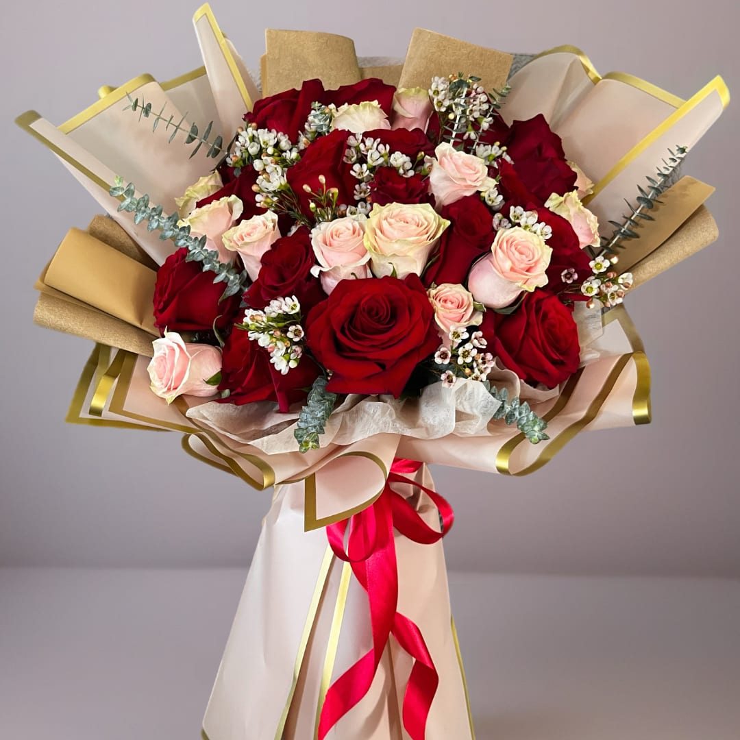 Bouquet of red and pale pink roses wrapped in cream paper with gold trim