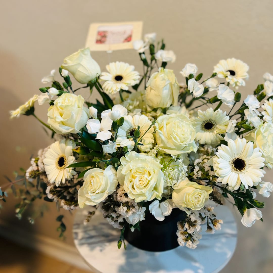 Cream roses and white daisies arranged in a black vase