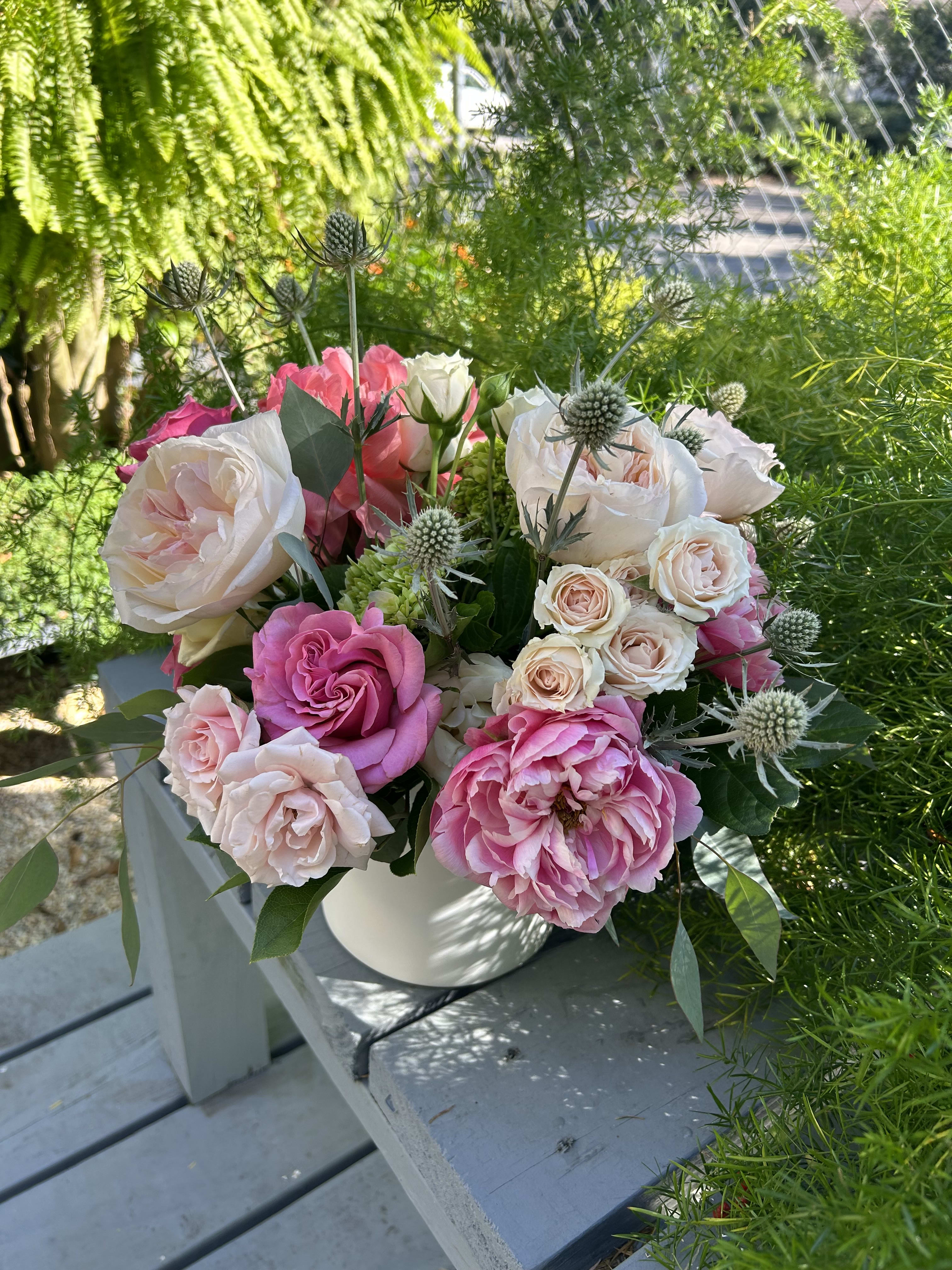 Pink and white roses in a white vase with spiky thistle accents