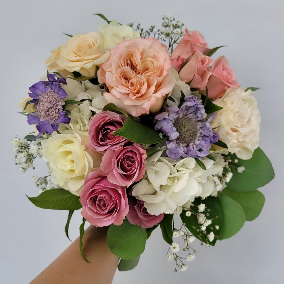 Handheld bouquet of pink, peach, white, and purple roses with small filler flowers