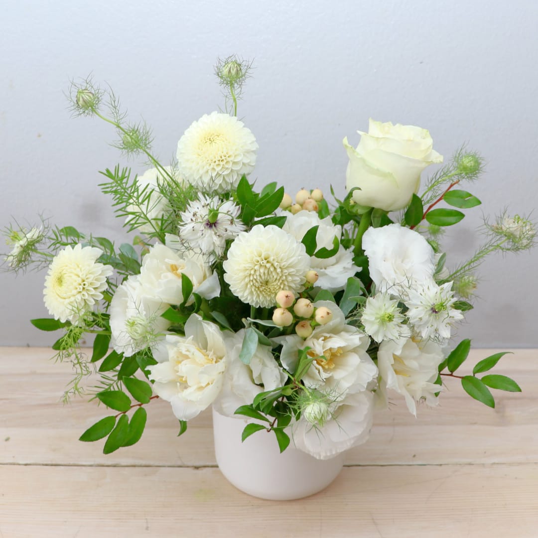 White floral arrangement in a white vase with roses and round blooms